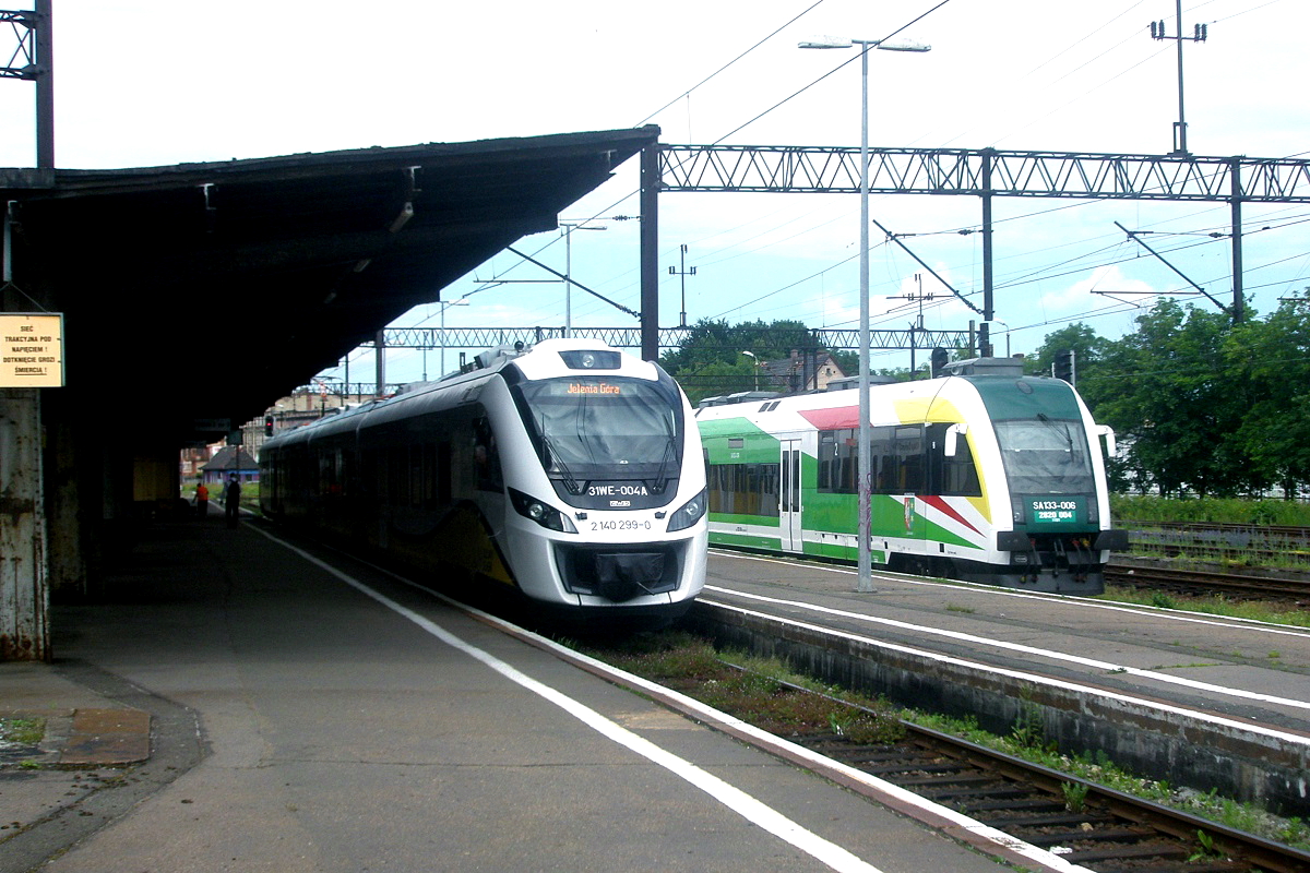 Am 22.06.2013 wartet der Flirt 3 140 299-0 der Kolej na Dolnym Slasku im Bahnhof Jelenia Gora/Hirschberg auf Fahrgäste. Nach der Regionalisierung sind die polnischen Wojwodschaften für den Regionalverkehr zuständig, in Niederschlesien wird er durch die Kolej na Dolnym Slasku betrieben. Neben dem Flirt 3 ist der Dieseltriebwagen SA 133-006 zu sehen, der zu einer zwischen 2006 und 2009 bei PESA gebauten Serie von 16 Triebwagen gehört. 
