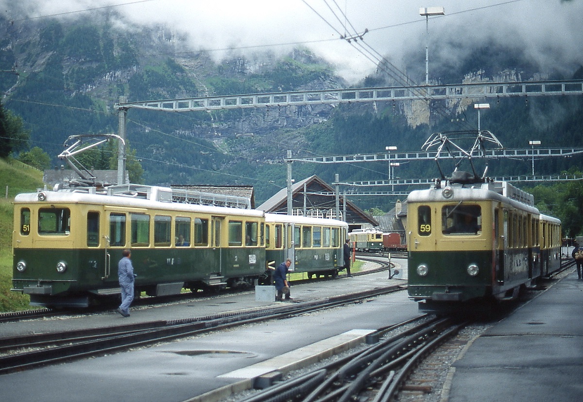 An einem regnerischen Junitag 1990 stehen zwei BDhe 4/4 mit unterschiedlichen Stromabnehmern im Bahnhof Grindelwald Grund