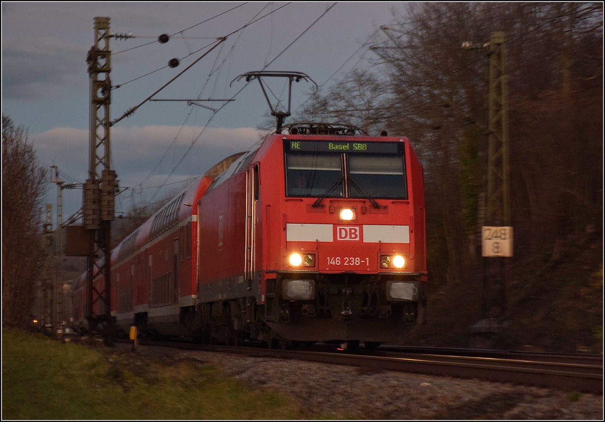 Bei Einbruch der Dunkelheit fährt der RE nach Basel mit der Schwarzwaldbahnlok 146 238 bei Bamblach vorüber. Dezember 2017.