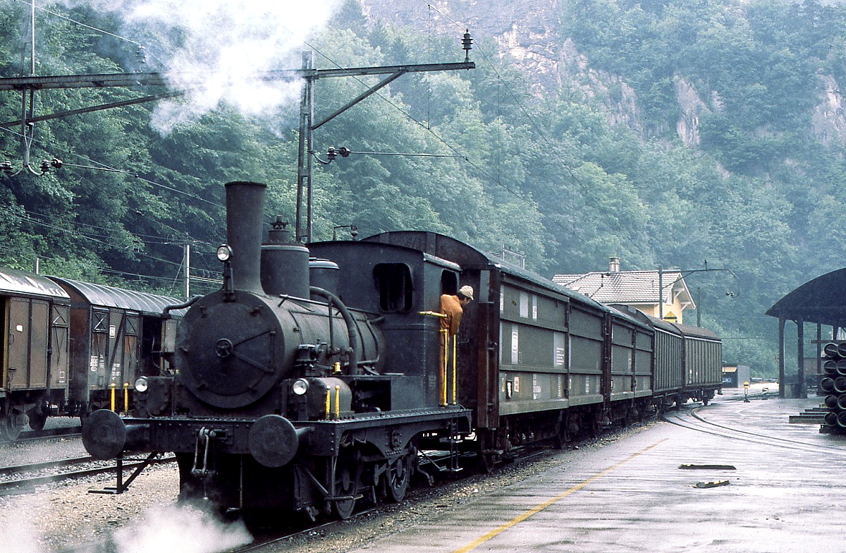 E 2/2 9 der von Roll-Werke in Choindez bei Rangierarbeiten im Juli 1983. Die Lok wurde 1911 von SLM gebaut (Fabrik-Nr. 2168) und direkt an das Werk geliefert, dort war sie bis in die 1990er Jahre im Einsatz, heute gehört sie zu La Traction. Von der Konstruktion her entspricht sie den 1881 an die Gotthardbahn gelieferten E 2/2 11 und 12. Bei dem Antrieb nach dem System Brown liegen die Zylinder über dem Umlaufblech, die Kraft wird durch Hebel auf das Triebwerk übertragen. Die Maschine besaß lediglich eine mechanische Bremse. Die Fotostelle war öffentlich zugänglich, der Weg zum im Hintergrund sichtbaren SBB-Bahnhof führte durch das Werksgelände.