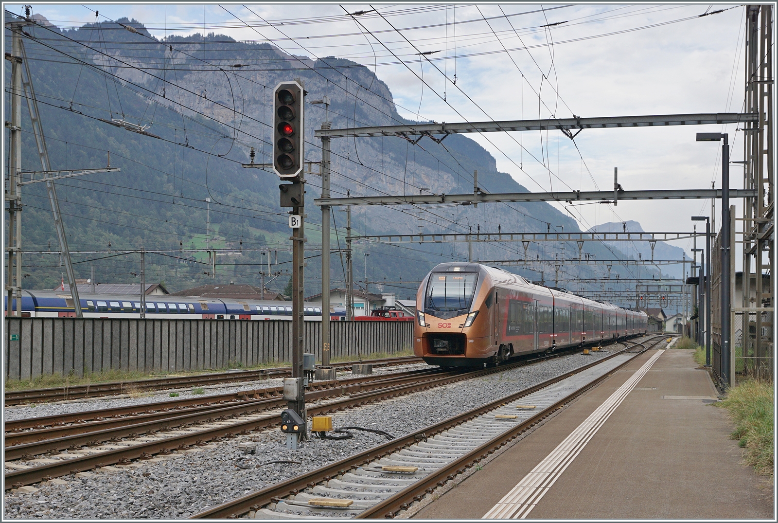 Der SOB  Traverso  RABe 526 209 als  Treno Gotthardo  von Basel nach Locarno erreicht Erstfeld. Im Hintergrund, hinter einer (unnützen) Lärmschutzwand rangieren SBB Aem 940 Züricher S-Bahn Doppelstock Wagen.

19. Oktober 2023