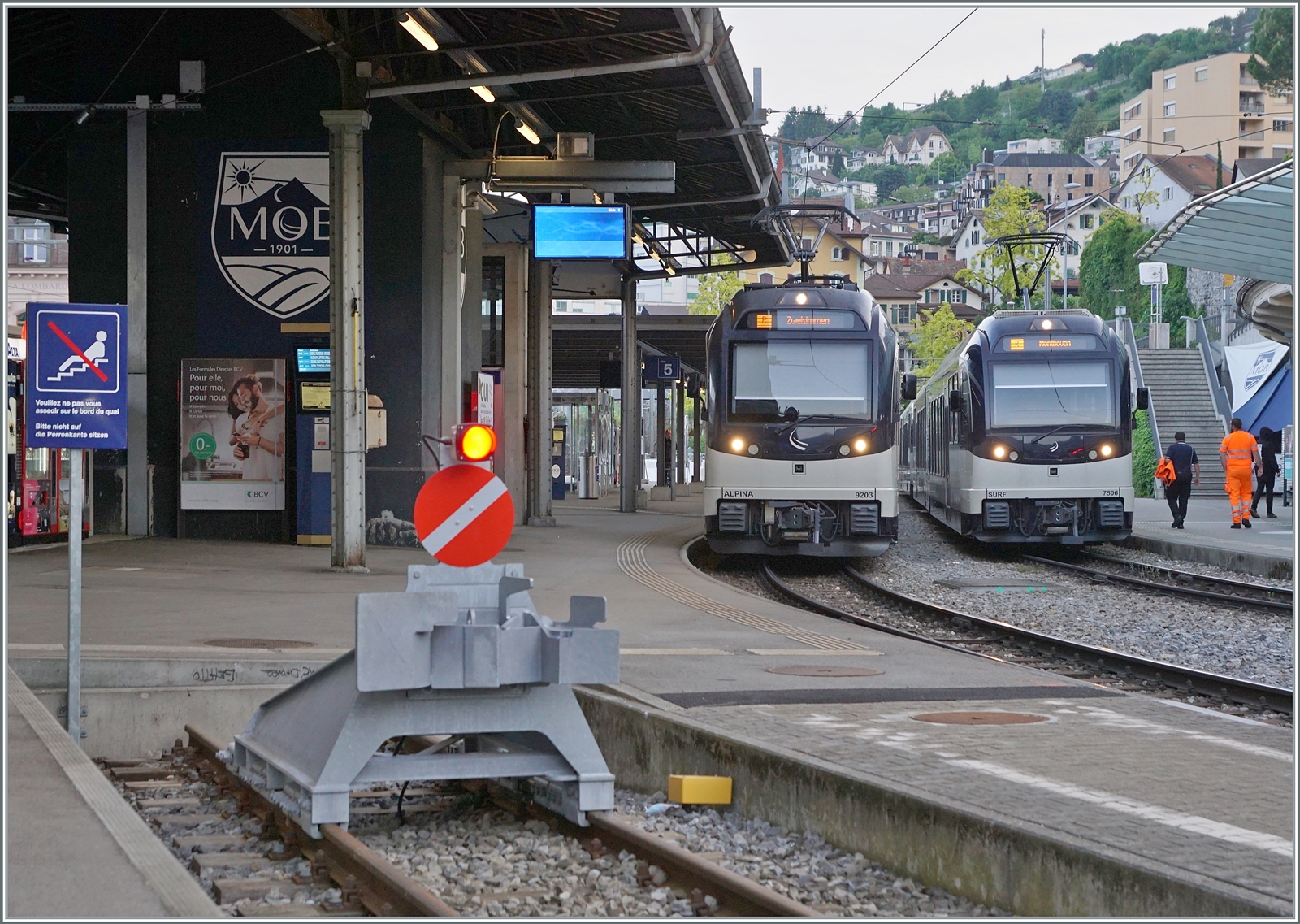 Während der MOB  Alpina  Be 4/4 9203 mit seinem Panoramic Zug auf die Abfahrt nach Zweisimmen wartet, steht ein CEV MVR ABeh 2/6 7506 (und ein weiterer) als Regionalzug nach Montbovon in Montreux. Zudem gibt es im Bild weiter Details zu sehen, wie z.B das Schild, welches verbietet an Bahnsteigkanten zu sitzen. 

23. Mai 2023