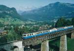 abde-88-mob/357059/mob-stilreiner-blauer-regionalzug-mit-dem MOB: Stilreiner blauer Regionalzug mit dem ABDe 8/8 4002 'VAUD' bei Passieren des Viadukts bei Gstaad im Juli 1991.
Foto: Walter Ruetsch