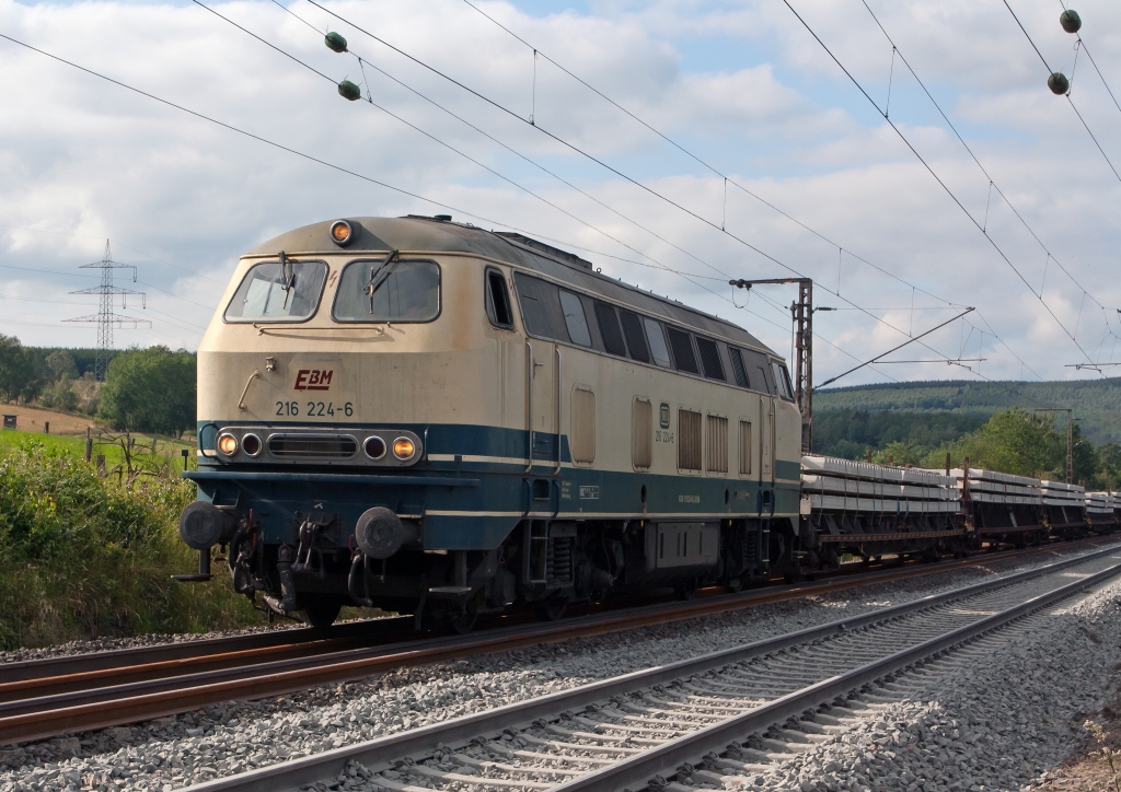 Die 216 224-6 der EBM Cargo (Gummersbach) kommt mit einem Schwellenzug am 29.07.2011 von Siegen ber das Baugleis in Wilnsdorf-Rudersdorf (KBS 445). Die Lok wurde 1968 bei Krupp unter der Fabriknummer 4885 gebaut.
Die Baureihe V 160 (ab 1968: Baureihe 216) war die erste Variante der V 160-Familie der Deutschen Bundesbahn, die im Nachkriegs-Neubauprogramm als einmotorige Grodiesellokomotive fr den mittelschweren Streckendienst projektiert wurde.
Angetrieben wird die Lok vom Dieselmotor MTU 16 V 538 / 653 TB 10 mit 16 Zylindern und einer Leistung von 1900 PS bei 1500/min. Die Leistung gelangt ber ein hydraulisches Getriebe mit zwei Wandlern und einer Kupplung und Gelenkwellen zu den Radsatzgetrieben in den beiden zweiachsigen Drehgestellen. Zustzlich zum Fahrdieselmotor ist ein kleiner Hilfsdieselmotor vorhanden, welcher beim Aufrsten -- insbesondere zum Betrieb des Dampfheizkessels -- und als Kompressor zur Luftversorgung genutzt werden kann.