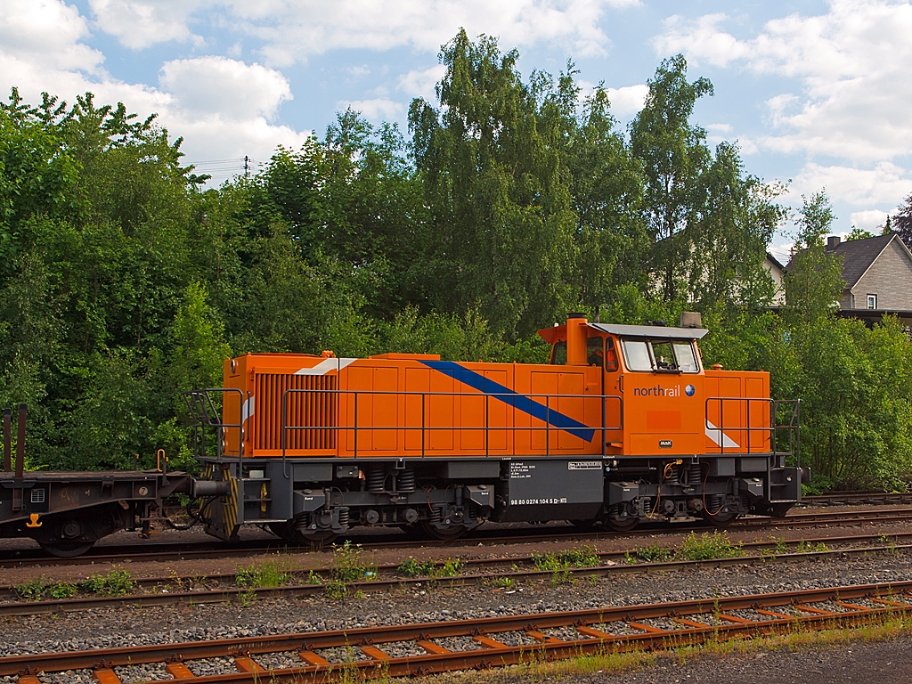 Im Bahnhof Herdorf hat am 06.06.2013 auf Gleis 4 die MaK G 1205 der northrail 274 104-5 (98 80 0274 104-5 D-NTS) mit leeren Sammnps-Schwerlastwagen noch Hp 0, bevor sie Richtung Betzdorf weiterfahren kann.
Die Lok wurde 1993 bei Mak in Kiel unter der Fabriknummer 1000892 fr Bayernwerk AG (BAG), Schwandorf  M 22 gebaut. Im Jahr 2002 kam sie dann zur OHE - Osthannoversche Eisenbahnen AG, Celle als  150007 , bis sie 2009 zur northrail kam.
