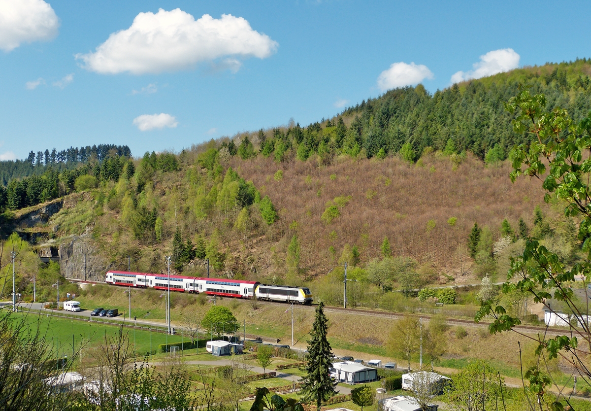 . Bereits um 11.06 Uhr tummelten sich die ersten Wolken am immer noch blauen Himmel, als der IR 3710 Luxembourg - Troisvierges, gezogen von der 3003, den Tunnel Scheidemhle verliess und den Camping Platz von Clervaux erreichte. 21.04.2014 (Jeanny)