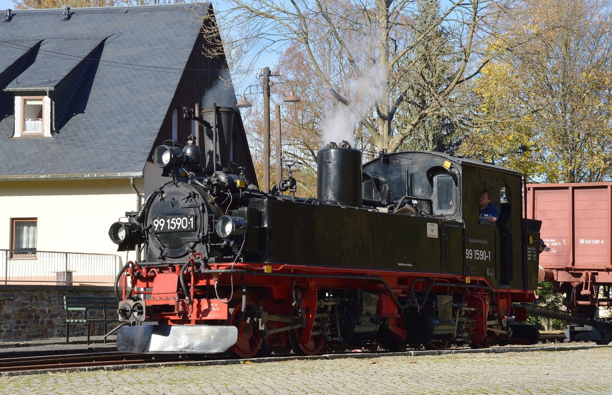 99 1590-1 wurde 1913 von der Sächsischen Maschinenfabrik, vormals Richard-Hartmann, in Chemnitz erbaut. Bis 1980 fuhr die Lok für die DR. Eine ihrer Stammstrecken war die Preßnitztalbahn. Neben dieser Bahn, fuhr die Lok auch auf der Strecke Wilkau-Haßlau - Carlsfeld, dort fuhr sie noch mit die Abbauzüge. Dann war sie noch auf dem Mügelner Netz zuhause. Im August 1992 erwarb die IG Preßnitztalbahn die Lok und ließ sie Betriebsfähig aufarbeiten. Seit Oktober 1994 steht die Lok wieder unter Dampf. Hier steht sie im Bahnhof Schmalzgrube vor einem Güterzug am 24.10.2015