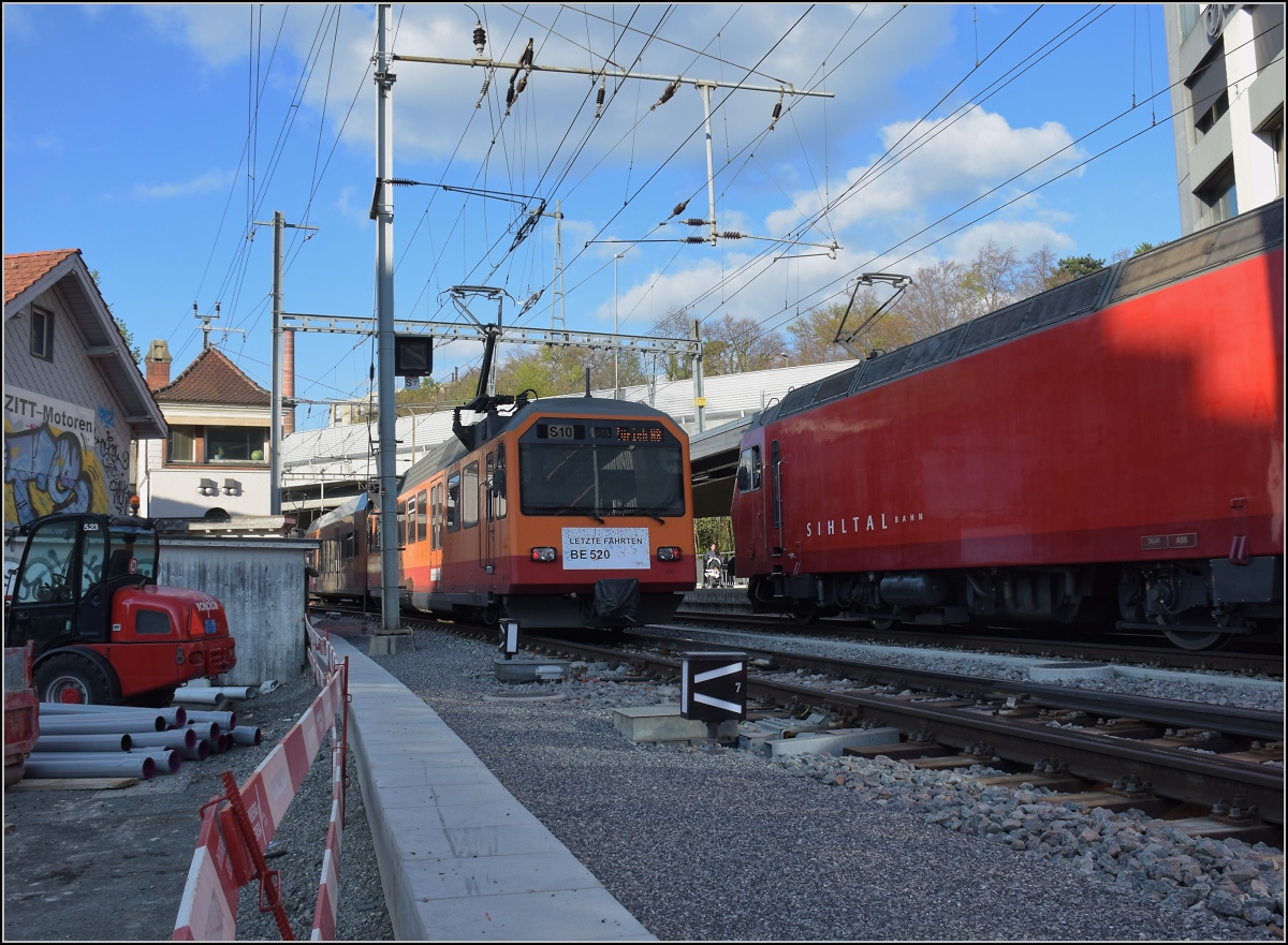 Abschied von einem Unikum, der Mehrsystemoberleitung in Zürich Giesshübel.

Hier in Giesshübel treffen Gleichstrom und Wechselstrom aufeinander. So weicht die 1,2 kV Gleichstromfahrleitung der Uetlibergbahn seitlich aus. Der Stromabnehmer geht knapp am Masten vorbei. Be 556 527, Be 556 526 und hinten Be 556 522 greifen mit gleich 6 Stromabnehmern den Strom ab. Rechts im Bild ist Re 456 106 der Sihltalbahn. April 2022.