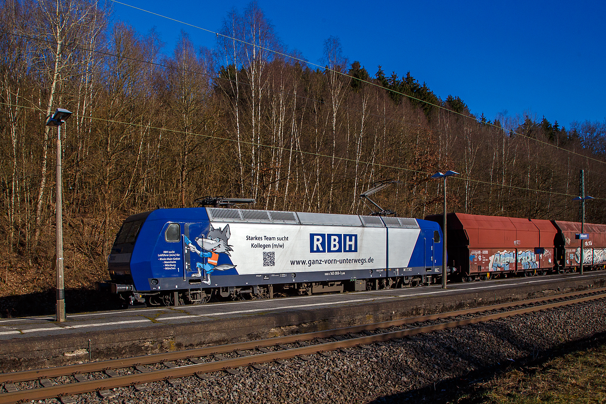 Auch wenn eine Lampenmast etwas stört, noch ein Seitenpotrait....
Die an die RBH Logistics vermietete 145 069-1 (91 80 6145 069-1 D-DB) der DB Cargo AG fährt am 01.03.2021, mit einem Schüttgutwagenzug (leere 4-achsige offene Schüttgutwagen mit schlagartiger Schwerkraftentladung der Gattung Falns 121), durch Dillbrecht an der Dillstrecke (KBS 445) in Richtung Siegen.

Die TRAXX F140 AC wurde 2000 von Adtranz in Kassel unter der Fabriknummer 33396 gebaut und an die DB geliefert, bis 2018 fuhr si für die DB Cargo und wurde dann an die RBH Logistics GmbH in Gladbeck vermietet und dort unter der internen Nummer RBH 228 geführt. 

Die RBH Logistics ist ein Tochterunternehmen der DB Cargo Deutschland AG und die Nachfolgegesellschaft von Werks-, Zechen- und Hafenbahnen im Raum der Bergwerksdirektion Recklinghausen. Durch die verschiedenen Firmenzusammenschlüsse und -aufteilungen ergab sich seit 1913 eine wechselvolle Geschichte. Das heute als Teil des Firmennamens genutzte Akronym RBH stand einige Jahre für die RAG-Bahn- und Hafenbetriebe und wurde beim Verkauf von dieser an die Railion Deutschland im Jahr 2005 beibehalten. Nach damaliger Angabe des neuen Eigentümers stehen die Buchstaben R, B und H nun für die Kernkompetenzen des Unternehmens: Eisenbahnverkehr (Rail), Binnenschifffahrt (Barge) und Hafenumschlag (Harbour).