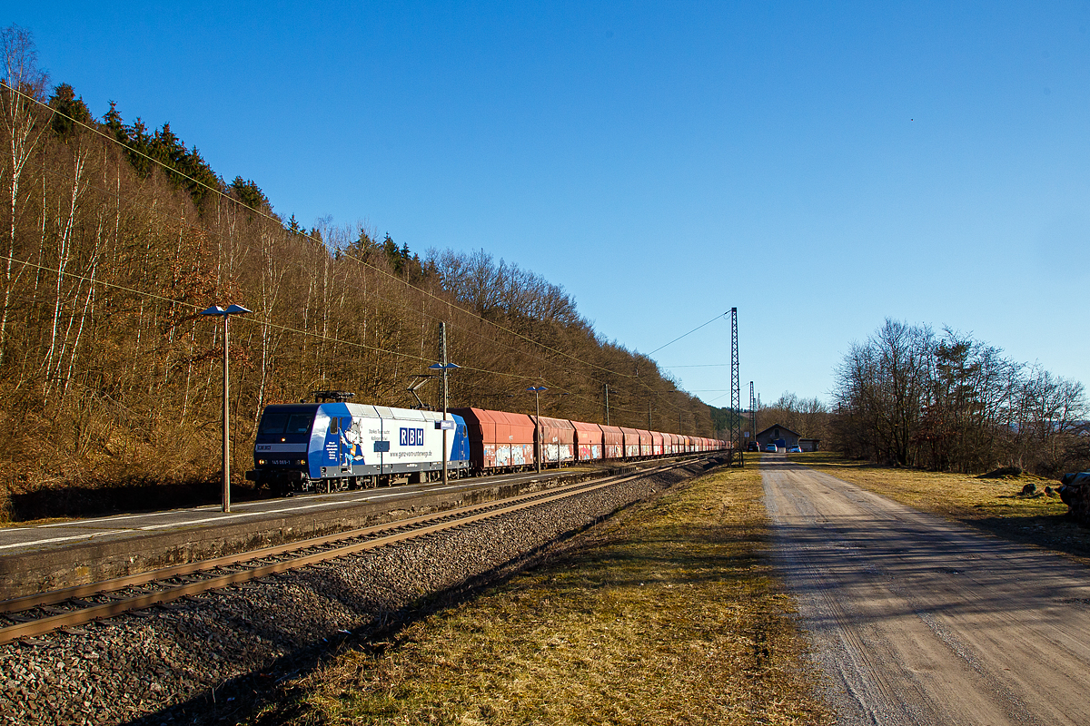 Auch wenn eine Lampenmast etwas stört....
Die an die RBH Logistics vermietete 145 069-1 (91 80 6145 069-1 D-DB) der DB Cargo AG fährt am 01.03.2021, mit einem Schüttgutwagenzug (leere 4-achsige offene Schüttgutwagen mit schlagartiger Schwerkraftentladung der Gattung Falns 121), durch Dillbrecht an der Dillstrecke (KBS 445) in Richtung Siegen.

Die TRAXX F140 AC wurde 2000 von Adtranz in Kassel unter der Fabriknummer 33396 gebaut und an die DB geliefert, bis 2018 fuhr si für die DB Cargo und wurde dann an die RBH Logistics GmbH in Gladbeck vermietet und dort unter der internen Nummer RBH 228 geführt. 

Die RBH Logistics ist ein Tochterunternehmen der DB Cargo Deutschland AG und die Nachfolgegesellschaft von Werks-, Zechen- und Hafenbahnen im Raum der Bergwerksdirektion Recklinghausen. Durch die verschiedenen Firmenzusammenschlüsse und -aufteilungen ergab sich seit 1913 eine wechselvolle Geschichte. Das heute als Teil des Firmennamens genutzte Akronym RBH stand einige Jahre für die RAG-Bahn- und Hafenbetriebe und wurde beim Verkauf von dieser an die Railion Deutschland im Jahr 2005 beibehalten. Nach damaliger Angabe des neuen Eigentümers stehen die Buchstaben R, B und H nun für die Kernkompetenzen des Unternehmens: Eisenbahnverkehr (Rail), Binnenschifffahrt (Barge) und Hafenumschlag (Harbour).