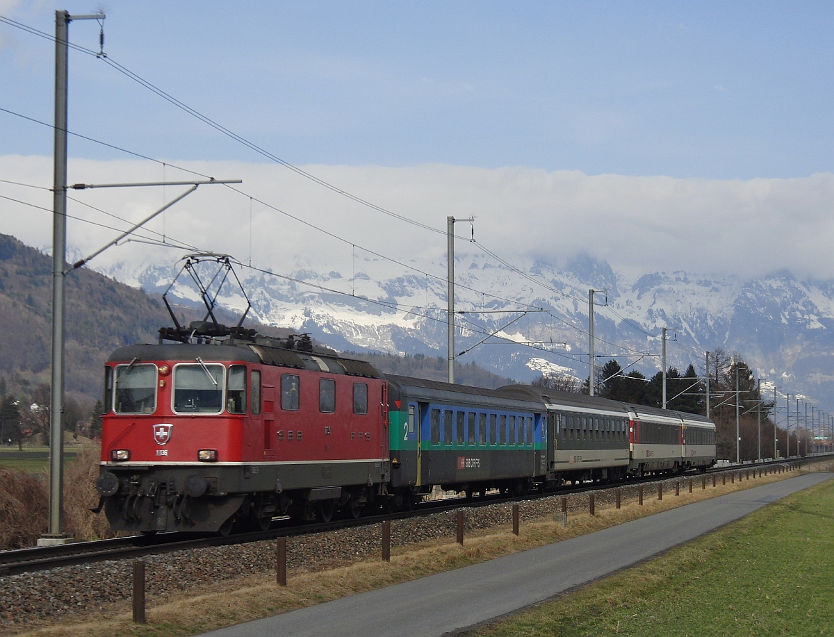 Bei Plattlis fährt Re 4/ II 11136 mit dem aus unterschiedlichen Wagen zusammengestellten RHEINTAL-EXPRESS RE 3811 von St. Gallen nach Chur am 06.03.2012 am Fotografen vorbei.