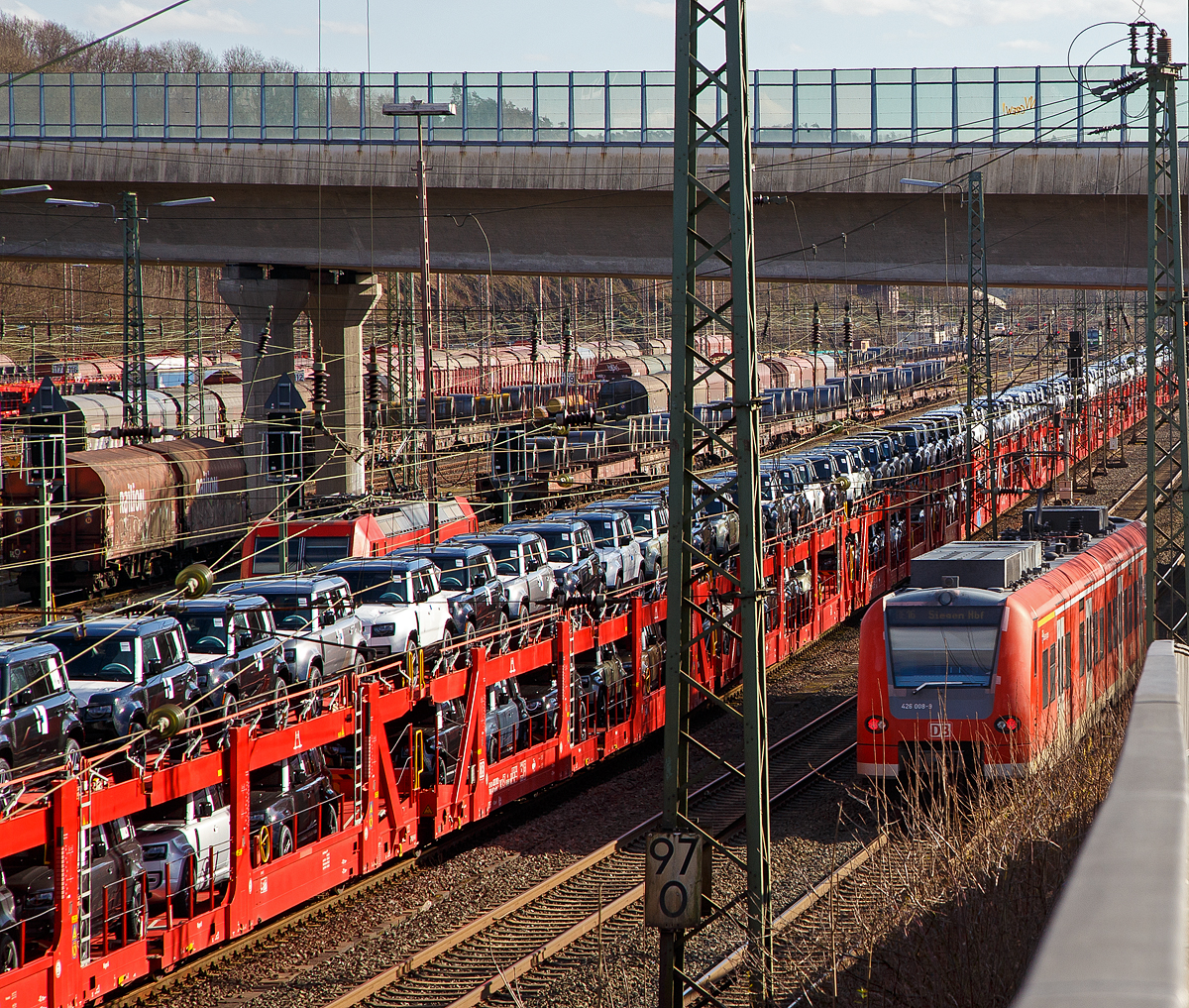 Blick auf den Rangierbahnhof (Rbf) Kreuztal am 23.02.2022, während vorne der zweiteilige DB Babyquietschie 426 508-8 / 426 008-9 „Besseringen“ (94 80 0426 508-8 D-DB und 94 80 0426 008-9 D-DB) der DB Regio, als RE 16  Ruhr-Sieg-Express  (Essen – Hagen – Siegen), weiter in Richtung Siegen fährt. Der Güterbahnverkehr in Richtung Hagen staute sich etwas in Kreuztal, da die Ruhr-Sieg-Strecke entlang der Lenne (durchs Sauerland) an diesem Tag nur eingleisig befahrbar war. So steht hier links die 185 053-6 mit einem sehr langen Autotransportzug und dahinter steht noch die 185 248-2.