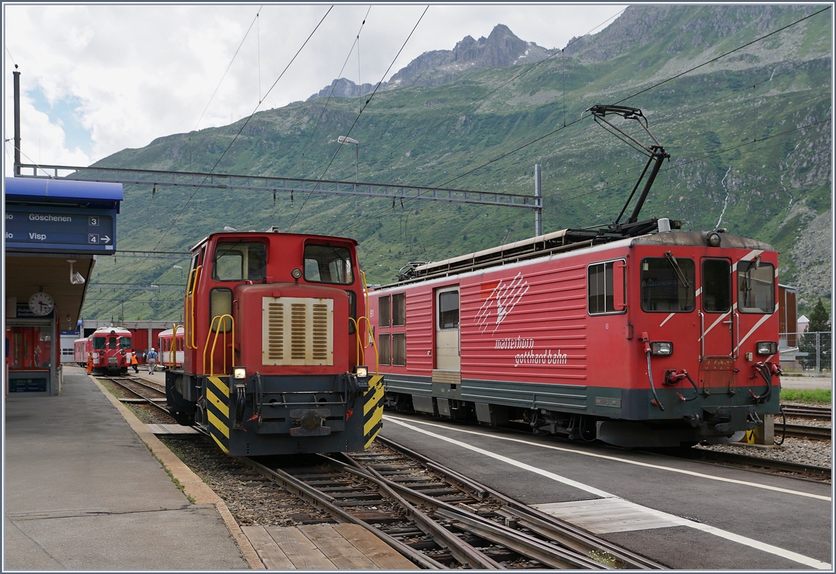 Da auf der steilen Schöllenen Bahn die Anhängelast begrenzt ist, werden jeweils in Andermatt die von Visp kommenden Verstärkungswagen abgehängt und dann gleich dem Gegenzug übergeben. 
Hier holt die  Schöma  Disellok nach der Ausfahrt des Zuges nach Göschenen die Wagen ab, während rechts der BDeh 4/4 54 (mit seinem Regionalzug nach Visp) für das Ankuppeln der Verstärkungswagen bereit steht.
28. Juli 2016