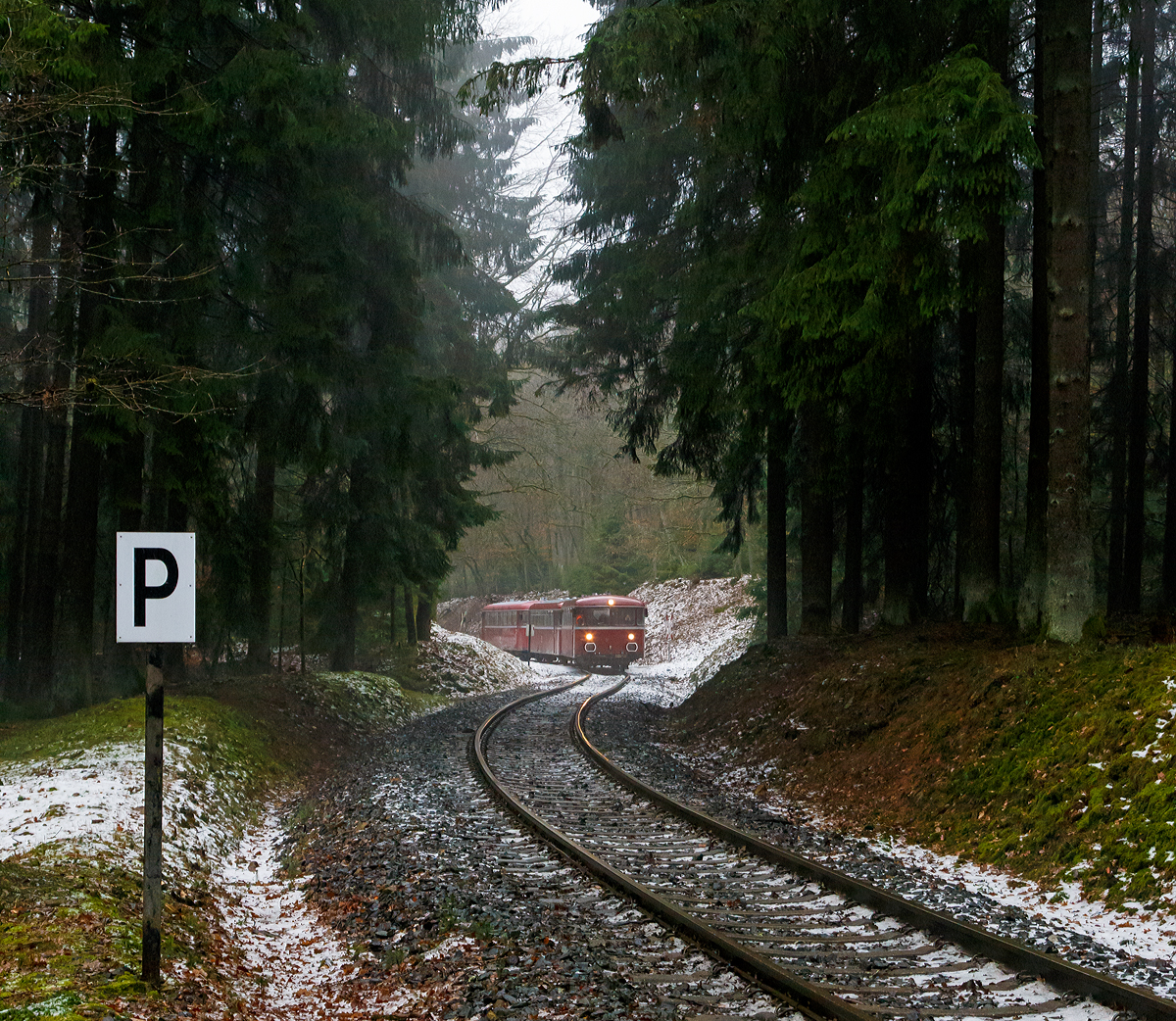 
Da kommen sie hinab vom Pfannenberg....
Eine Schienenbusgarnitur der VEB Vulkan-Eifel-Bahn Betriebsgesellschaft mbH auf Sonderfahrt (bestehend aus 798 670-6, 998 863-5 und 796 784-7) fährt am 26.01.2019 von der ehem. Grube Pfannenberger Einigkeit  (heute Sitz der Schäfer Werke) hinab zur Spitzkehre Pfannenberg bei Neunkirchen-Salchendorf. 

Die Garnitur befährt die priv. Strecke der Kreisbahn Siegen-Wittgenstein (Betriebsstätte Freien Grunder Eisenbahn - NE 447). Heute gibt es zwischen Herdorf und der Grube Pfannenberger Einigkeit noch jeden Werktag Güterverkehr, obwohl die Erzgrube Pfannenberger Einigkeit ihren Betrieb im April 1962 aufgegeben hat. An ihrer Stelle benötigen seitdem die Schäfer Werke KG den Anschluss für die Zulieferung von Stahl Coils sowohl als Rohstoff als auch für ihren Handel mit deren Zuschnitten nach Kundenwunsch.
