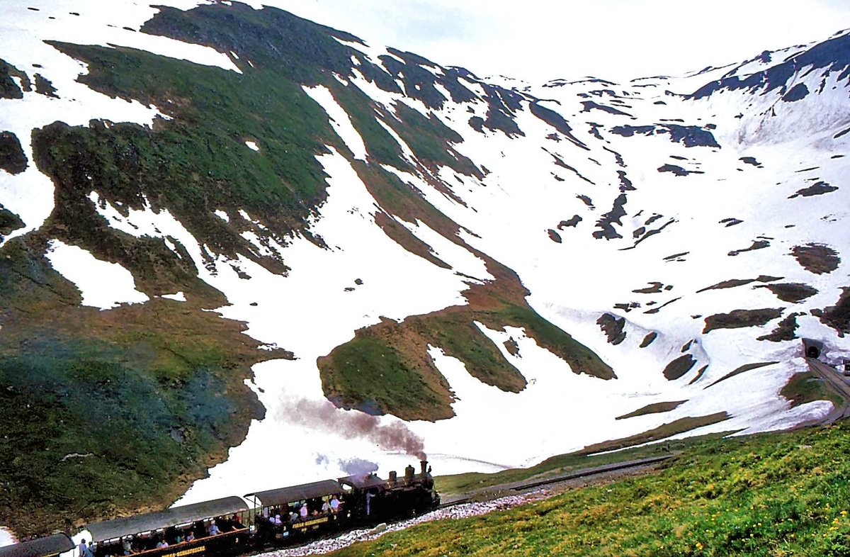 Dampfbahn Furka Bergstrecke: Lok 1 fährt unterhalb der Station Furka ins Bild hinein. 1.Juli 1995  