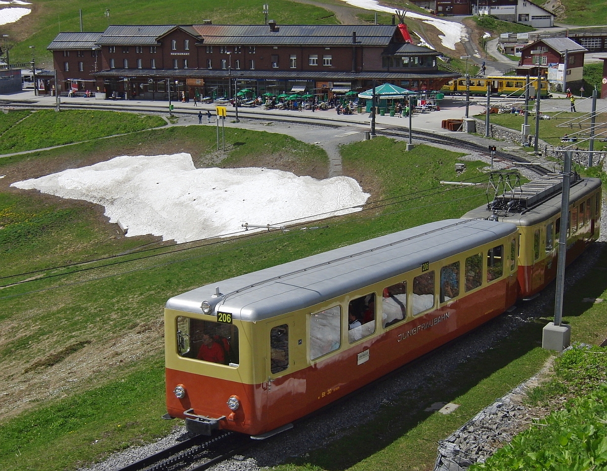 Der 1961 in Betrieb genommene Triebwagen 206 der Jungfraubahn kurz nach dem Start im Bahnhof Kleine Scheidegg (15.06.2013). Rechts hinter dem Gebäude ist ein Teil des gelb-grünen Triebwagens der Wengernalpbahn zu sehen, mit der die Gäste von Lauterbrunnen aus anreisen.