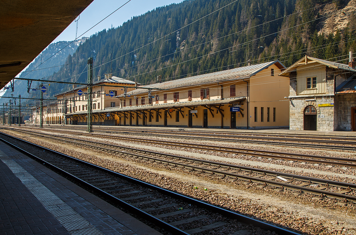 Der Bahnhof Brenner (Stazione di Brennero) am 27.03.2022, der Blick vom Bahnsteig 6 in sdlicher Richtung aufs Empfangsgebude. 

Der Bahnhof Brenner (italienisch Stazione di Brennero) befindet sich an der Brennerbahn. Er ist der Grenzbahnhof zwischen Nord- und Sdtirol und so zwischen sterreich und Italien. Der Bahnhof liegt auf der Passhhe des Brenners (1.370 m). Dieser enge, hchstgelegene Abschnitt des Wipptals bietet zwischen steilen Berghngen nur wenig Platz fr das kleine Passdorf und wird zu groen Teilen von Verkehrsinfrastrukturen wie dem Bahnhof, der A22/A 13 und der SS 12/B 182 beansprucht. Der Bahnhof befindet sich fast zur Gnze auf dem Gebiet der Sdtiroler Gemeinde Brenner bzw. auf italienischem Staatsgebiet, das hier auch auf Flchen nrdlich der Wasserscheide bergreift. Lediglich kleinere Teile im nrdlichen Bereich des Bahnhofs gehren zur Tiroler Gemeinde Gries bzw. zum sterreichischen Staatsgebiet.

Der von Wilhelm von Flattich entworfene Bahnhof Brenner wurde 1867 zusammen mit dem gesamten Abschnitt der Brennerbahn zwischen Innsbruck und Bozen in Betrieb genommen, damals gehrte ja noch alles zur Doppelmonarchie sterreich-Ungarn. An den planenden Ingenieur des Projekts, Carl von Etzel, erinnert eine Bronzebste am Bahnhofsgelnde. Die ursprnglich relativ unbedeutende Station erfuhr 1888 aufgrund der hohen Fahrgastzahlen der neuen Strecke eine erste Erweiterung.

Die Annexion Sdtirols durch Italien infolge des Ersten Weltkriegs vernderte die Situation grundlegend, da nun die neue Staatsgrenze ber den Brenner verlief. Die Teilstrecken Innsbruck–Brenner und Verona–Brenner wurden von nun an von zwei verschiedenen Verwaltungen betreut, die sich zudem noch in feindseliger Haltung gegenberstanden. 1930 wurde ein kompletter Neubau des Empfangsgebudes eingeweiht.

In der Bildmitte an den OL-Auslegern sieht man die Fahrleitungssignale, 
auf der Spitze stehenden Quadrat mit blauem Hintergrund und weiem Rand in wei angebracht, hier der waagerechte weie Streifen zeigt so das „Signal - El 4 - Bgel ab (Stromabnehmer tief)“. Das Signal kennzeichnet die Stelle, an der der Oberleitungsbgel einer Ellok vollstndig abgesenkt sein muss. Damit der Lokfhrer mit dem Absenken rechtzeitig beginnt, ist 250m vor diesem Signal das Signal El3 aufgestellt. 

Hier endet das in sterreich (BB) bliche Stromsystem mit 15 kV, 16,7 Hz Wechselstrom, etwas sdlicher beginnt dann das in Italien (RFI) bliche Stromsystem mit 3 kV Gleichstrom. Es zeigt aber hier nicht die Landesgrenze, die liegt weiter nrdlicher (in meinem Rcken). 
