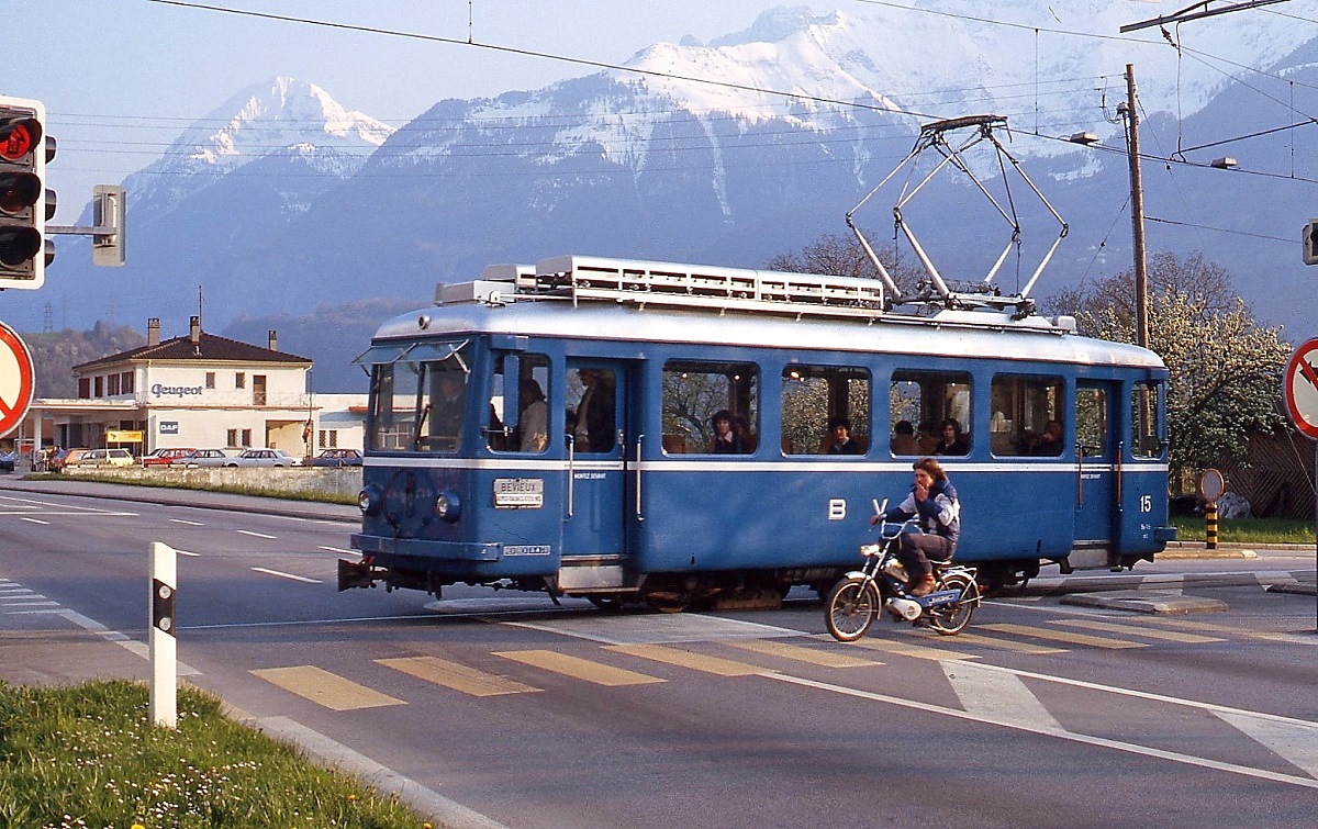 Der Be 2/3 15 der BVB an der Kreuzung der Avenue de la Gare mit der Kantonsstraße 9, eine grandiose Bergkulisse - und ein junger Mopedfahrer, der sich mit ins Bild drängt. Die ampelgeregelte Kreuzung wurde inzwischen zu einem Kreisverkehr umgebaut.