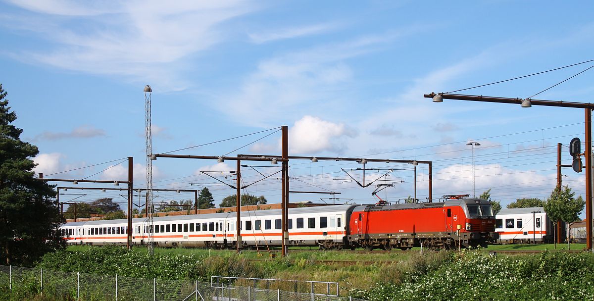 Der IC 1197 Kopenhagen Hbf - Hamburg Hbf mit DSB EB 3211 an der Spitze hat am 15.08.2023 in Pattburg/Padborg bereits über eine Stunde Verspätung und blockiert somit das Gleis 2 für den Gegenzug IC 1192, der bereits am Einfahrtsignal wartet, da auf Gleis 1 noch die Gumminase nach Aarhus steht.
Um 17.10 Uhr fährt IC 1197 vorsichtig Richtung Hamburg Hbf aus, kommt aber am Ausfahrtsignal wieder zum Stehen. Zwischenzeitlich hatte die Gumminase das Gleis 1 geräumt und man sieht im Hintergrund den letzten Wagen des IC 1192. Zwei ellokbespannte IC in unterschiedlichen Richtungen hatte ich bislang noch nicht gleichzeitig Pattburg gesehen