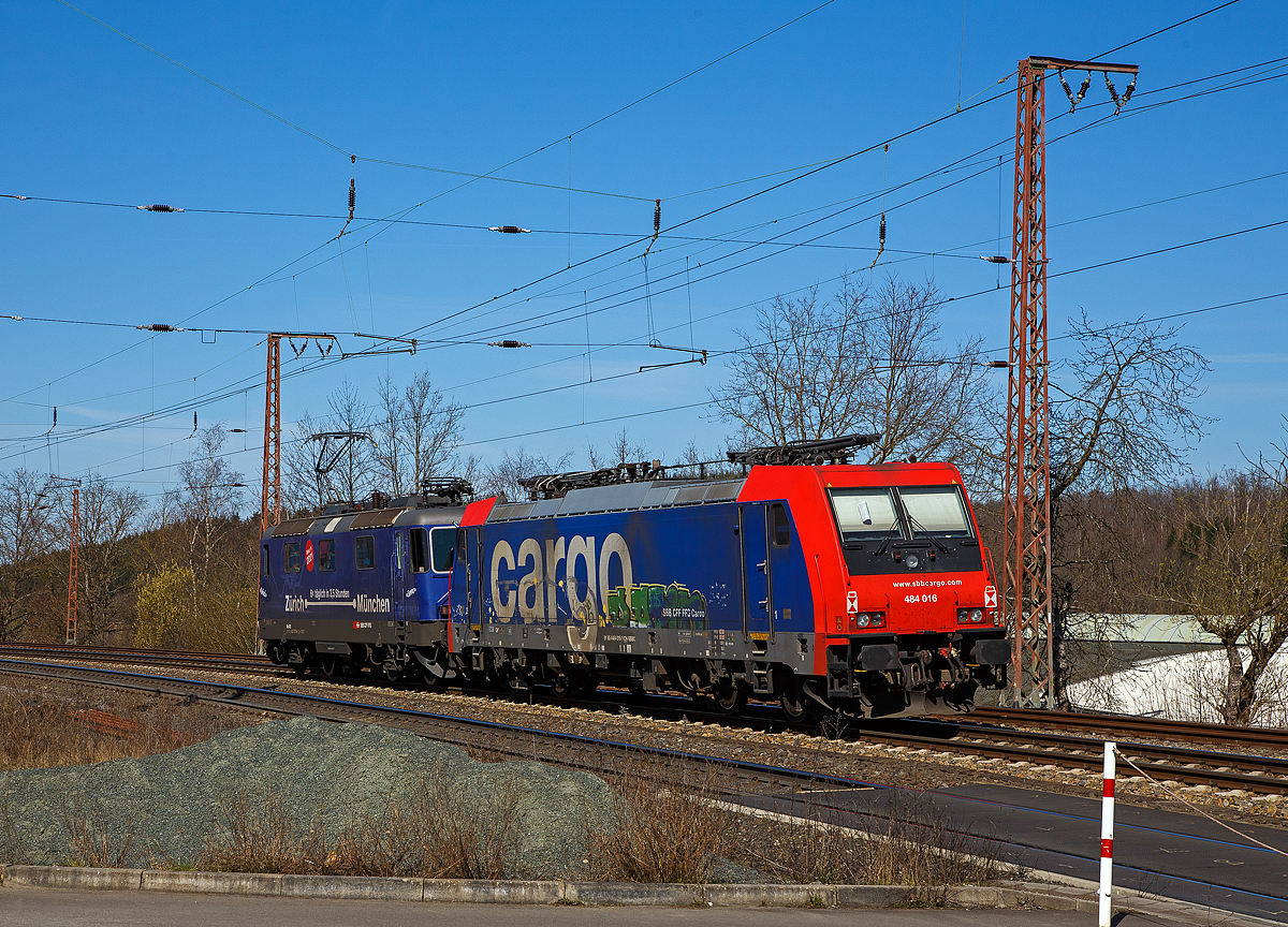 Die SBB Cargo Re 484 016-1(91 85 4484 016-1 CH-SBBC), ex E 484.016 SR, eine TRAXX F140 MS, geschleppt am Haken der SBB Cargo Re 421 371-6 (91 85 4421 371-6 CH-SBBC), ex Re 4/4 II 11371, mit Werbung Zürich – München 6 x täglich in 3,5 Stunden, erreichen am 30.03.2021 Rudersdorf (Kr. Siegen) und haben nun ermal Hp 0, bevor es in Richtung Siegen weitergeht. 

Eine SBB Cargo Re 484 wie die 016-1 kann man eigentlich Deutschland nur mit viel Glück sehen, denn sie haben nur die Zulassungen für die Schweiz und Italien. Sie haben keinen Stromabnehmer mit breiterer Wippe gemäß deutscher Vorschrift, auch die die deutsche Zugsicherung Indusi fehlt ihnen. Der Lz war auf dem Weg nach Krefeld.

Lebensläufe:
Die Re 421 371-6 wurde 1983 von der SLM Winterthur (Elektrik BBC/ SAAS) unter der Fabriknummer 5235 gebaut und als Re 4/4 II 11371 an die SBB geliefert. Im Jahr 2002 erfolgte der Umbau zur Re 421 für die SBB Cargo (Einsatz auch in Deutschland). Die zugelassene Höchstgeschwindigkeit für die Schweiz beträgt 140 km/h und für Deutschland 120 km/h.

Die Re 484 016-1 eine Bombardier TRAXX F140 MS wurde 2004 von Bombardier in Kassel unter der Fabriknummer 34009 gebaut und an die SBB Cargo AG, als E 484.016 SR geliefert.