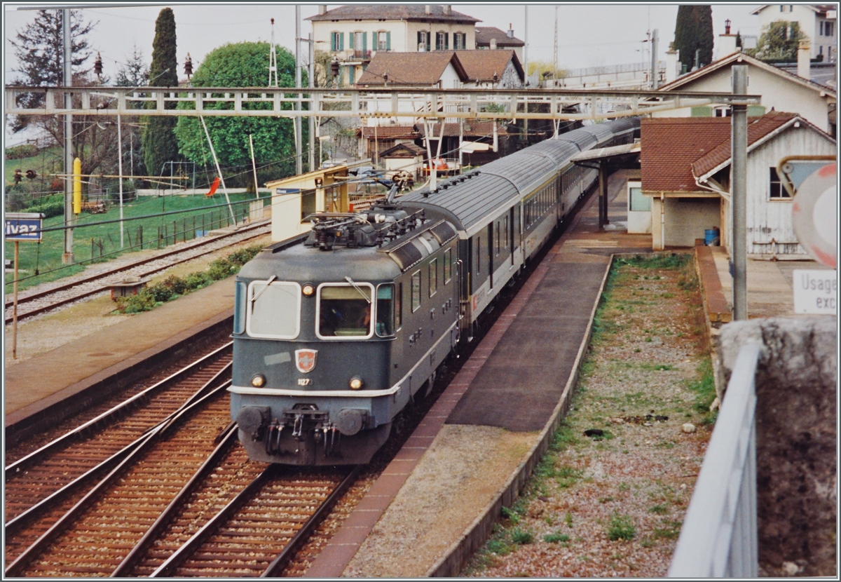 Die SBB Re 4/4 II 11273 fährt mit einem Schnellzug nach Birg durch den Bahnhof von Rivaz. 
Während das Gleis zum Schuppen bereits abgebaut ist, existiert das Seeseitige Abstellgleis noch. 

Analogbild vom April 1994

