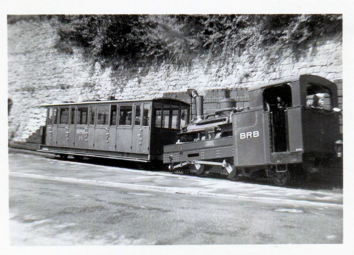 Ein altes Bild von der Lok 5 (mit Wagen 1). Der Zug steht vor der charakteristischen Brikett-Wand, aus der früher die Kohle für die Lok genommen wurde. Die Lok hat noch den alten Führerstand mit dem offenen Fenster und der Schaufel ausserhalb dieses Fensters. Auch kann man ganz rechts unten noch die Petrollampe erkennen. 1.Juli 1961  
