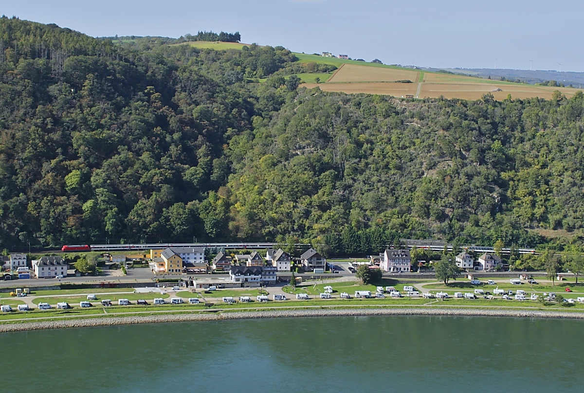Ein Blick am 11.10.2023 vom Loreleyfelsen nach Westen auf die rechtsrheinische Mittelrheinstrecke und den von eine 101 gezogenen EC 9 (Hamburg-Altona - Zürich Hbf.), der Aussichtswagen befindet sich an vorletzter Stelle des Zuges. Der am Rheinufer gelegene Campingplatz ist ein insbesondere bei Niederländern beliebtes Ausflugsziel.