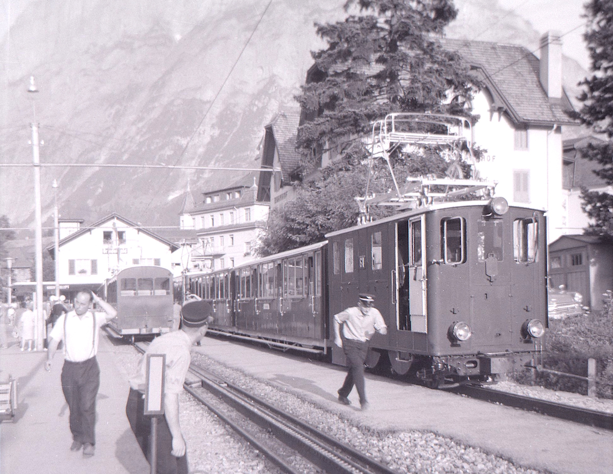 Ein hektischer Nachmittag in Grindelwald. Die Ankunft weiterer Züge wird erwartet, so hat einer der Züge seinen hinteren Wagen im Stationsgleis gelassen und ist mit dem vorderen Wagen ins damals noch existierende Ausziehgleis gefahren. Jetzt muss die Weiche für den kommenden Zug schleunigst umgestellt werden. Im Sommer 1962. 