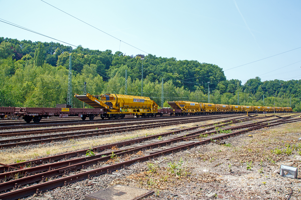 
Ein Zug mit Plasser & Theurer Materialfrder- und Siloeinheiten MFS 40 der eurailpool GmbH abgestellt am 04.07.2015 in Betzdorf/Sieg.

Arbeitsweise:
Am Boden jedes MFS 40 befindet sich ein ber die ganze Wagenbreite gehender Frdergurt und an der Stirnseite ein breites Abgabefrderband.

Das Aushubmaterial fllt von der Maschine kommend auf den Bodengurt, wird zum Abgabefrderband gebracht und an die nchste Einheit bergeben. Dieser Vorgang wiederholt sich, bis die am weitesten entfernte Siloeinheit erreicht wird. Bei dieser vordersten Siloeinheit ist das Abgabefrderband an der Stirnseite des Wagens in Ruhestellung.

Auch der Frdergurt am Boden des Wagens ist so lange in Ruhestellung, bis die obere Fllgrenze erreicht ist. Dann wird der Frdergurt in Bewegung versetzt und dadurch im bergabebereich freier Raum fr die weitere Beladung geschaffen. Durch die dem Flltempo angepasste Geschwindigkeit des Frdergurts wird die ganze Siloeinheit vollstndig gefllt. Das Fassungsvermgen einer Siloeinheit betrgt 40 Kubikmeter.

Nach Fllung einer Teilgruppe des Abraumzuges kann diese von der Restgruppe abgekuppelt werden, zu einer Entladestelle gefahren und dort entleert werden, whrend die Restgruppe des Abraumzuges noch befllt wird. Das Entladeband ist nach beiden Seiten ausschwenkbar. Die Entladung kann dabei auf einer Deponie erfolgen oder es knnen LKW's oder Waggons am Nachbargleis beladen werden. Smtliche Einheiten des Abraumzuges knnen durch Ausschwenken aller Abgabefrderbnder gleichzeitig entleert werden. Die Entladung eines Wagens dauert ungefhr fnf Minuten.
