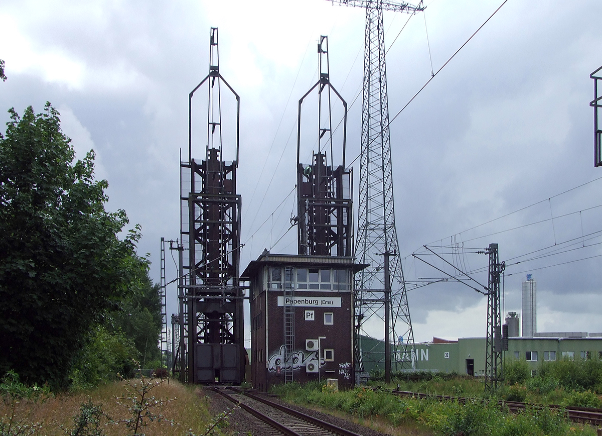 
Gleich vor dem Bahnhof Papenburg (Ems) befindet sich die Eisenbahnklappbrücke über den Papenburger Sielkanal, davor noch das Fahrdienstleiterstellwerk Papenburg (Ems) „Pf“, hier am 20.06.2009.

Hier ist die Brücke, für die freie Schiffsdurchfahrt, gerade oben.