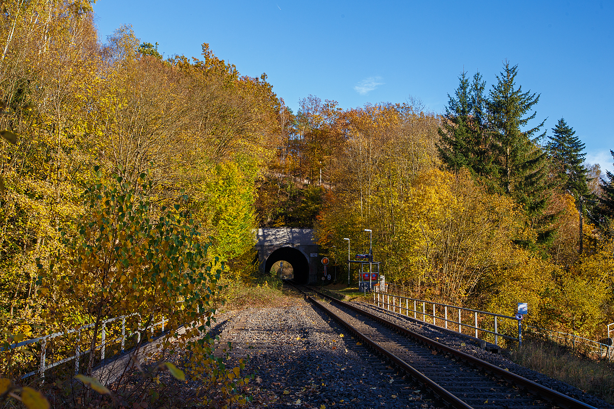 Herbstzeit im Hellertal.....
Der Bedarfs-Haltepunkt Herdorf-Knigsstollen dahinter der Herdorfer Tunnel (137 m lang) bei km 88,6 der Hellertalbahn - KBS 462 (Bahnstrecke Kln-Deutz – Betzdorf – Herdorf – Haiger – Gieen). Vorm Tunnel das (Form) Vorsignal fr das Einfahrtsignal vom Bahnhof. Es zeigt Vr 0 „Halt erwarten“ (Die runde Scheibe steht senkrecht, der Flgel zeigt er senkrecht nach unten). 

Die Hellertalbahn wurde als Teil der Deutz-Gieener Eisenbahn gebaut, die in den Jahren 1859 bis 1862 als Hauptbahn von Kln-Deutz nach Gieen in mehreren Etappen durch die Cln-Mindener Eisenbahn errichtet wurde. Aufgrund der Verkehrsentwicklung und der militrischen Bedeutung 1870/71 wurde die Strecke 1871 zweigleisig ausgebaut. 

Damals war diese Strecke noch die Hauptstrecke. Der Niedergang der Hellertalstrecke begann im Jahre 1915, als die durch den Rudersdorfer Tunnel verlaufende Alternative erffnet wurde, erst ab da gab es eine direkte Verbindung zwischen Siegen und Haiger. Sowohl der hochwertige Reiseverkehr als auch der Groteil des Gterverkehrs nutzten nunmehr die direkte und gnstiger trassierte Dillstrecke in Richtung Gieen und weiter ins Rhein-Main-Gebiet. 

Im Hellertal wurde aber noch Eisenerz abgebaut und auf die Bahn verladen. Auch gab es in Herdorf eine Stahlhtte. So war der Niedergang des Siegerlnder Erzbergbaus Anfang der 1960er Jahre dann der groe Niedergang der Stecke. Zudem wurden die Ruhr-Sieg- , die Sieg- und die Dillstrecke elektrifiziert. So wurde die Strecke Mitte der 1960er Jahre als Nebenstrecke zurckgestuft, folgte im Jahre 1965 die Demontage des zweiten Gleises im Bereich Herdorf–Haiger. Im Jahr 1987 wurde das zweite Gleis auf dem Abschnitt Betzdorf–Herdorf stillgelegt. Hier im Bild kann man (links) noch das zweite Gleis erahnen.

Heute erinnern nur noch die durchgehende Kilometrierung von Kln-Deutz und die gemeinsame Streckennummer an die alte Streckenfhrung.