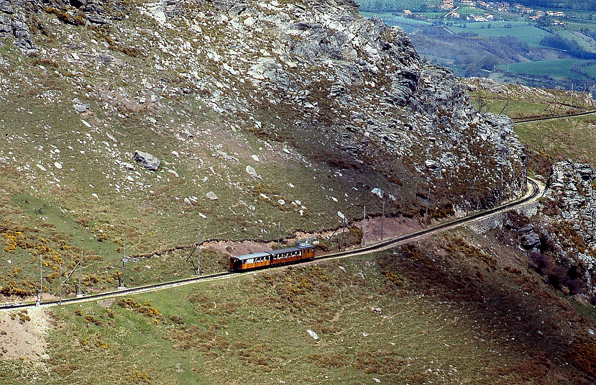Im April 1986 schiebt eine der von SLM gebauten Lokomotiven einen Zug der Chemin de Fer de La Rhune hinauf zum Gipfel. Die Bergspitze ist auch auf einem Wanderweg erreichbar, dort begegnete man damals immer wieder der mit weißer Farbe auf Steinblöcken angebrachten Inschrift  3+4=7 , ein Hinweis auf die von vielen Einheimischen als Einheit betrachteten 3 in Frankreich und 4 in Spanien gelegenen baskischen Provinzen.