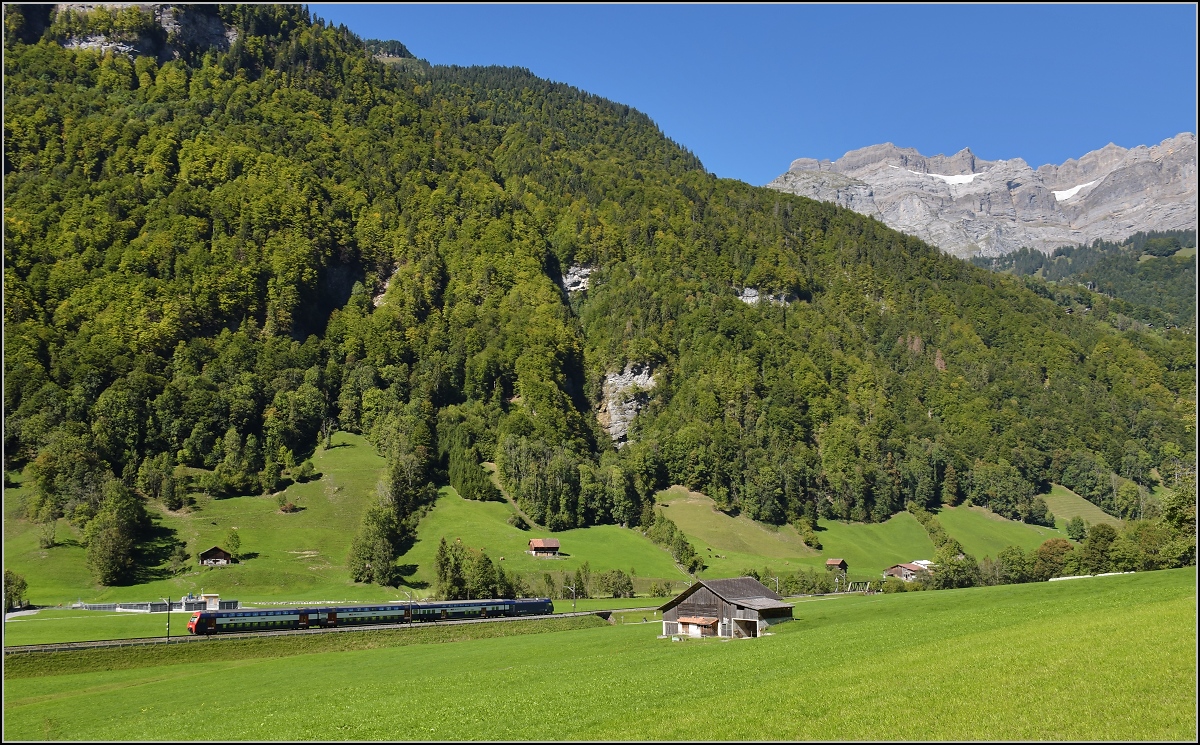 Im tiefeingeschnittenen Tal der Linth zeigt sich ein unbekannter Zug der S-Bahn Zürich mit Re 450 in ganz besonderem Licht. Im Hintergrund erhebt sich das prominente Glärnisch-Massiv. Diesbach, September 2019.