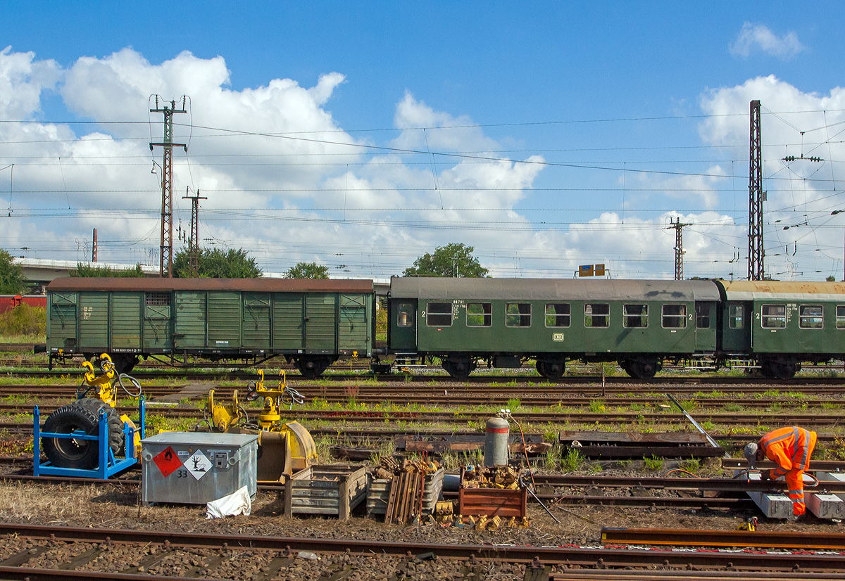 In Hanau am 27.08.2014 aus einem Zug heraus:
Links der zweiachsige ehemaliger Bahnpostwagen der Deutschen Post (DP) der DDR, 75 80 9229 054-6 D-MH, ex 50 50 09-10 076-7, ex DEW 1264 Post aa-c, ex DP/DR 83 076, ex Post 2ss-t (Deutschen Bundespost), der Museumseisenbahn Hanau e.V. (frher Dampfbahnfreunde Kahlgrund e.V.).

1983/84 importierte die DP aus Rumnien 140 zweiachsige Bahnpostwagen, die fr den Rollbehlterverkehr in schnellfahrenden Reisezgen (D-, E-, Post- und Gex-Zge) bestimmt und dementsprechend mit Dampfheizleitung, Zugsammelschiene und mit Bremsen der Bauart KE-GP A ausgerstet waren. Die zulssige Hg betrug 120 km/h. Nach bernahme und Umzeichnung in Post 2ss-t/12 im Jahre 1990 trennte sich die Deutsche Bundespost bis 1994 von diesen Wagen. Im Wandel des Gesamtdeutschen Bahnverkehrs war kein Platz mehr fr Bahnpostwagen. Innerdeutsch wird heute die Post mit LKW´s transportiert.

TECHNISCHE DATEN Bahnpostwagen:
Hersteller: MEVA in Turnu Severin (Rumnien), heute Astra Rail Industries
Baujahr: 1984
Spurweite: 1.435 mm
Anzahl der Achsen: 2
Lnge ber Puffer: 14.270 mm
Achsabstand: 8.000 mm
Hchstgeschwindigkeit: 100
Eigengewicht: 13.200 kg
Ladegewicht: 22 t
Bremse: KE-GP


Und rechts der dreiachsige B3yg ex DB Umbauwagen, ex DB 88 701 Ffm, der Museumseisenbahn Hanau e.V., kurzgekuppelt mit dem ex DB 88 166 Ffm.

Der Umbauwagen wurde 1957 vom AW Hannover aus dem Untergestell des Abteilwagen C3yg-*/54 (ex DB 049 655, ex DB Opp 70037, ex DRB Opp 847), der 1903 von der Waggonfabrik Breslau gebaut wurde, umgebaut.

Bei der DB war er von 1957-1966 als 88 701Ffm der Gattung B3yg-54 und von 1967 bis 1977 der Gattung B3yg761 unterwegs, bis 1990 war er Bahnhofswagen Heilbronn, spter ging er zu den Dampfbahnfreunde Kahlgrund e.V., seit 2010 hat er die NVR-Nr. 75 80 2329 040-9 D-MH. Der Wagen wurde im Frhjahr 2020 optisch und technisch aufgearbeitet und komplett neu lackiert. Er bildet mit dem B3yg-54 Wagen 88 166 Ffm eine Einheit als kurzgekuppeltes 3yg-Prchen.

TECHNISCHE DATEN Umbauwagen:
Umbauer: AW Hannover
Umbaujahr: 1957
Spurweite: 1.435 mm
Anzahl der Achsen: 3
Lnge ber Puffer: 13.300 mm
Achsabstand: 7.500 mm (2x 3.750 mm) 
Hchstgeschwindigkeit: 100
Eigengewicht: 18.300 kg
Sitzpltze: 62
