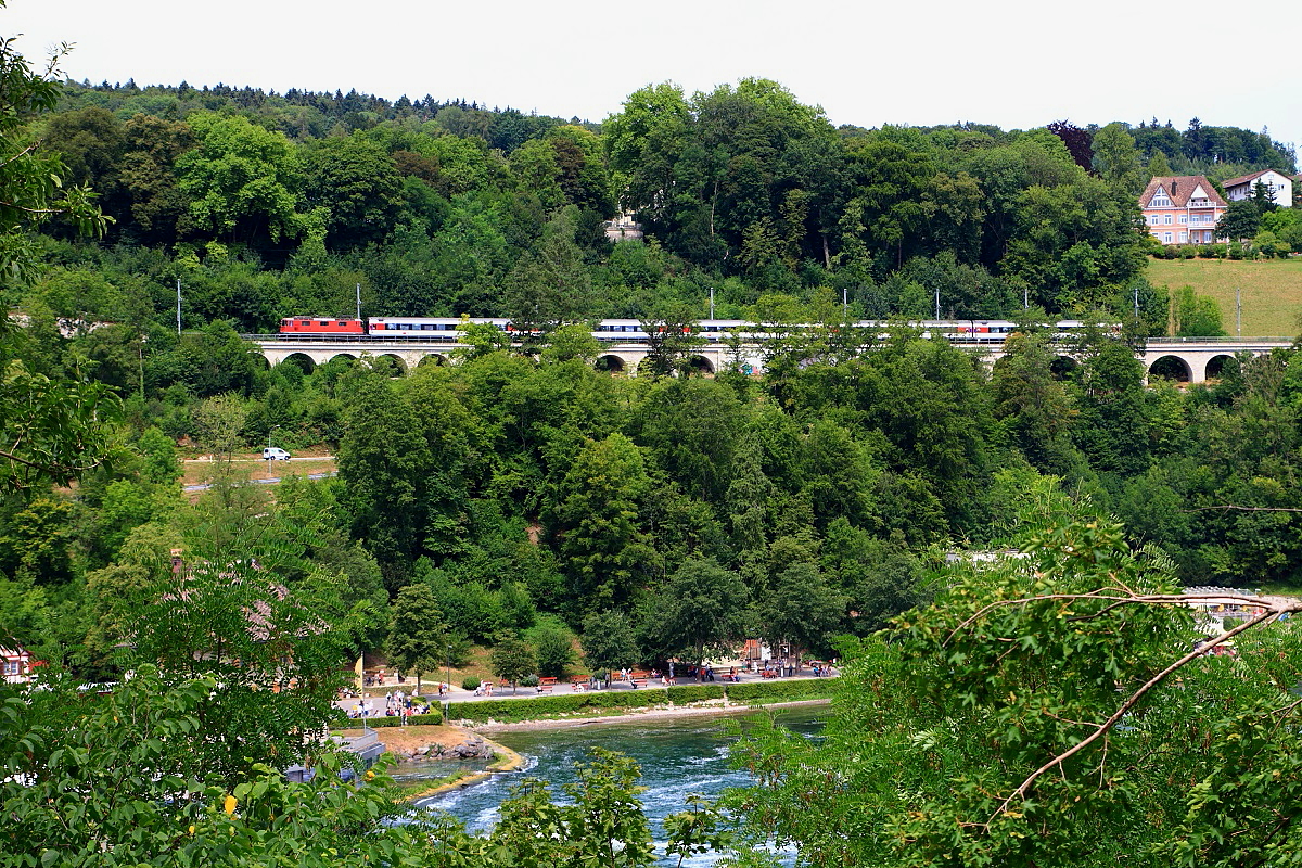 Mit einem EC nach Zürich ist eine Re 4/4 II am 26.07.2015 oberhalb des Rheinfalls unterwegs, die Aufnahme entstand vom Bahnsteig des Haltepunktes Schloss Laufen aus