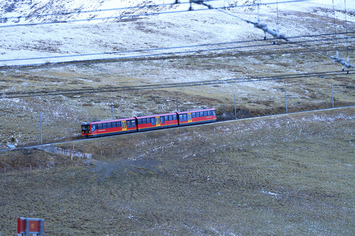 Nach dem ersten Schneefall kommt Jungfraubahn Triebzug 221 in verzuckerter Landschaft zur Kleinen Scheidegg herab. 14.Oktober 2021. Uebrigens: Es war gar nicht so einfach, die drei Teile (einzeln) dieses Zuges über die WAB von Grindelwald Grund her heraufzubringen, weil die beiden Endwagen sich innen auf gar kein Drehgestell abstützen; nur der Mittelteil hat beiderseits ein Drehgestell.  