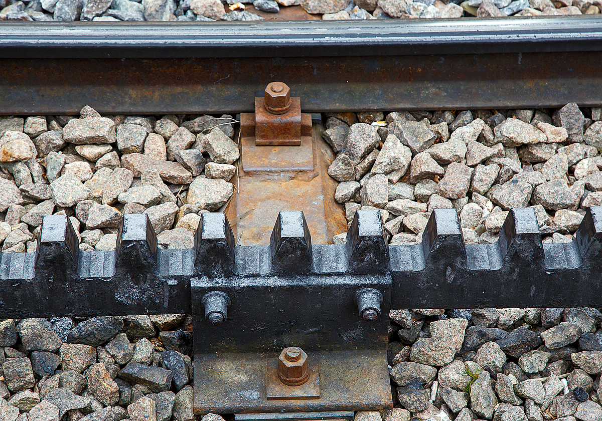 Nochmal im Detail, Gleis der Dolderbahn hier am 06.06.2015 an der Bergstation. 

Die Dolderbahn ist eine Privatbahn in der Stadt Zürich. Die Zahnradbahn erschließt (seit 1973, davor Standseilbahn) das Dolder-Gebiet im Quartier Hottingen ab der Haltestelle Römerhof am Römerhofplatz auf 444 Metern über Meer und endet in der Station Dolder auf dem Adlisberg auf 606 Metern über Meer. 

Die Bahn ist in der Spurweite1.000 mm (Meterspur) mit dem Zahnstangensystem von Roll ausgeführt. Die Zahnstangen sind hochliegend (über der Schienenoberkante). 
System Von Roll:
Die von der Firma Von Roll (heute Tensol) entwickelte Zahnstange ist nur dem Namen nach eine Lamellenzahnstange, nämlich eine einlamellige. Sie hat dieselbe Zahnteilung (100 mm) wie die Riggenbach'sche und die Strub'sche Zahnstange. Von letzterer unterscheidet sie sich in der Grundform: einfaches Breitflach-Profil anstatt einer Keilkopfschiene ähnliches Profil. Die Von Roll Zahnstange kommt in erster Linie bei Neubauten sowie als preisgünstiger Ersatz alter Zahnstangen nach den Systemen Riggenbach oder Strub zur Anwendung. Sie ist zwar dicker (30–80 mm, je nach Zahndruck) als eine der Lamellen nach Abt, doch ihre Biegsamkeit ist ausreichend, um flexibler als die Originale nach Riggenbach oder Strub anwendbar zu sein. Sie kann auch durchgehend verschweißt werden. Zur Befestigung auf den Schwellen dienen besondere Profilstahl-Sättel.

Die Systeme Von Roll, Riggenbach und Strub können miteinander kombiniert werden, d.h. in einer Zahnradbahn können Zahnstangen nach allen drei Systemen verbaut sein. Wobei man heute eigentlich aus Kostengründen nur noch Von Roll-Zahnstangen verbaut, da diese Lamellenzahnstangen auf einer automatischen Spezialmaschine präzis und wirtschaftlich hergestellt werden.