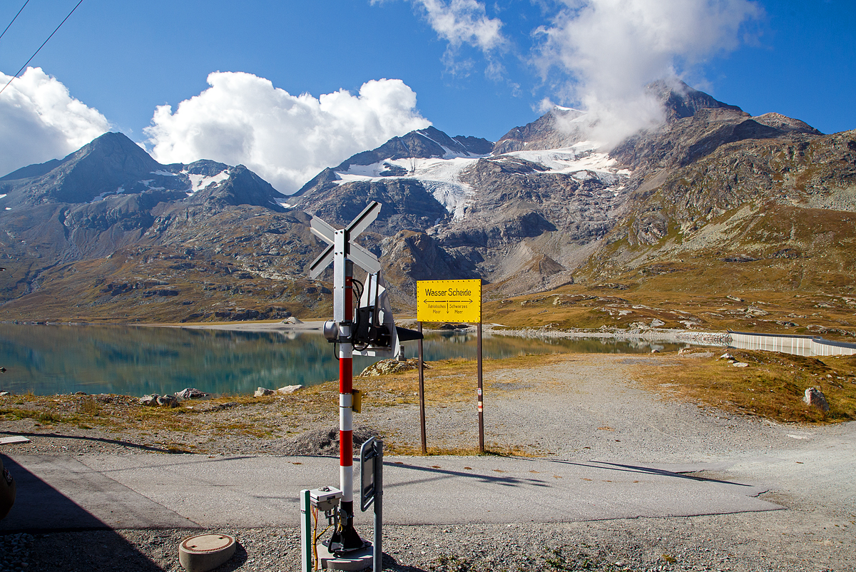 Nun erreichen wir am 06.09.2021den Lago Bianco auf einer Höhe von 2.223 Metern über Meer. 

Hier oben bei der Staumauer befindet sich auch zugleich die Wasserscheide zwischen Donau und Po. In Richtung Süden (Tirano) fließ das Wasser in den Po und somit ins Mittelmeer, in Richtung Norden (St. Moritz) fließ das Wasser über den Inn in die Donau und somit ins Schwarze Meer.

Der Lago Bianco ist ein Stausee am Berninapass zwischen dem Valposchiavo und dem obersten Seitental des Engadins, dem Val Bernina, in der Schweiz. Er liegt damit auf der Grenze zwischen den Bernina- (westlich) und Livigno-Alpen (östlich). Früher bestanden im Gebiet des heutigen Stausees zwei natürlichen Seen, der größere Lago Bianco, , und der kleinere südlich anschließende Lago della Scala. In den Lago Bianco mündeten mehrere kleine Bergbäche von den Höhen der Umgebung. Die beiden Gewichtsstaumauern Scala (Südseite) und Arlas (Nordseite) wurden zwischen 1910–1911 errichtet, so dass sich ein Stausee mit einem Volumen von 18,6 Mio. m³ bildete.

Unmittelbar am Nordende des Lago Bianco liegt die kontinentale Wasserscheide zwischen den Einzugsgebieten des Po und des Inn-Donau-Flusssystems. Wenige Meter nördlich des Lago Bianco liegt der Lago Nero (Schwarzsee) am Oberlauf des Berninabaches, dem folgt dann der kleinere Lago Pitschen (Pitschensee).
