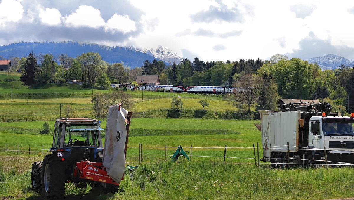 Palézieux Village: Blick von der Broyetallinie (die Fahrleitungsmasten sind hinter den Fahrzeugen vorn sichtbar) auf die Hauptstrecke Lausanne - Fribourg - Bern, wo gerade ein neuer Doppelstockzug (Serie 502) durchfährt. 20.Mai 2021  