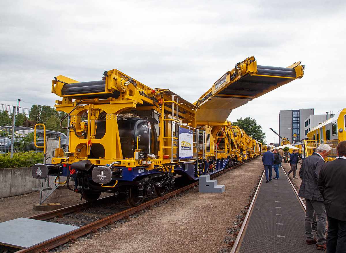 Plasser & Theurer präsentierte auf der iaf 2022 in Münster (hier am 31.05.2022) die Plasser MaterialTransferUnit / Materialfördereinheit aufgebaut auf einen Standard Containertragwagen der Gattung Sgnss 60´ (hier auf 37 81 4565 020-6 A-PLA der Franz Plasser Vermietung von Bahnbaumaschinen GmbH, Purkersdorf). 

Die Maschine wurde 2022 von Plasser & Theurer in Linz (A) unter der Maschine-Nr. 7191 gebaut. Sie ist eine Erweiterung des Materialkreislaufs, für Umladen, Beladen und Durchfördern von Schüttgut

Ausstattung und Aufbau:
• Modularer Aufbau nach Anforderung Umladen, Beladen, Durchfördern
• Flexible Schüttgutlogistik mit großer Abwurfweite ohne äußere Abstützung, Schwenkförderband mit einer Ausladung bis zu 6.870 mm, Transportsicherung für Schwenkförderband
• Beladen von Schüttgut durch konventionelle Baumaschinen, wie Bagger
• Durchfördern von Schüttgut in der MFS-Förderstraße mit Funktionsraum
• Modularer Aufbau auf Standard Containertragwagen (Sgns 60') als Trägerfahrzeug und Modultragrahmen 20´
• Autarke Energieversorgung zur flexiblen Einreihung  in eine Förderstraße, u.a. mittels Dieselmotor EURO V und Hydrauliknotpumpe
• Durchgehende selbsttätige Bremse
• Aufstieg mit Geländer
• Funkfernsteuerung für Schwenkförderband
• LED-Beleuchtung
• Funktionsraum mit Sozialeinrichtung
• Wassersprühanlage zur Staubreduktion
• Wassertank 3.000 1
• Zugwarnanlage mit Druckluft-Warnanlage System Zöllner
• Werkzeugschrank

TECHNISCHE DATEN:
Spurweite: 1.435 mm (Normalspur)
Anzahl der Achsen:  4 in 2 Drehgestellen
Länge über Puffer: 19.740 mm
Drehzapfenabstand: 14.200 mm
Achsabstand im Drehgestell: 1.800 mm
Eigengewicht Modul: 52.600 kg
Eigengewicht Tragwagen: 25.800 kg
Max. Achslast: 20 t
Höchstgeschwindigkeit: 100 km/h
Zugelassen für Streckenklasse: C2 oder höher
Kleister befahrbarer Gleisbogen: R 75 m
Bremse: KE-GP-A (K)
Bremssohle: J 816 M
Handbremse: Ja
Ausladung Schwenkförderband bis zu: 6.870 mm

Die Einheit wurde hier auch so präsentiert wie sie eingereiht werden könnte, dahinter (in Arbeitsrichtung davor) sieht man eine Materialförder- und Siloeinheit MFS 120 und Bettungsreinigungsmaschine RM 85-750 N.