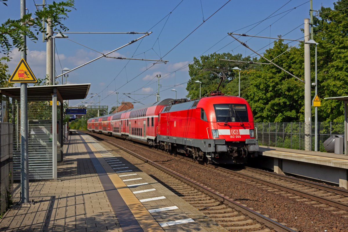 Seit einiger Zeit finden sich in den Doppelstock-Garnituren auf der Linie RE1 zunehmend Wagen, die nicht zum eigentlichen Fahrzeugpark dieser Linie geh�ren. In diesem Zug, der am 10.09.2021 von 182 009 geschoben in Erkner h�lt, fallen die zwei letzten Wagen nicht nur farblich aus dem Rahmen. Mit einer zugelassenen H�chstgeschwindigkeit von 140 km/h bremsen sie den eigentlich mit 160 km/h betriebenen Zug ein wenig aus.