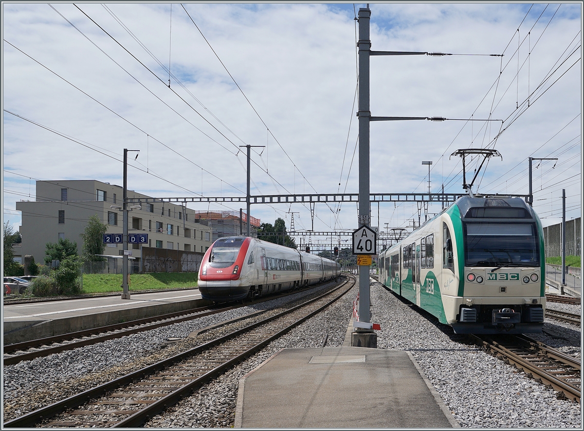 Während der SBB ICN RABe 500 017  Willi Ritschard  auf dem Weg von Genève-Aéroport nach Zürich Moregs erreicht, verlässt ein BAM Regionalzug nach Bière den Bahnhof.

2. August 2021