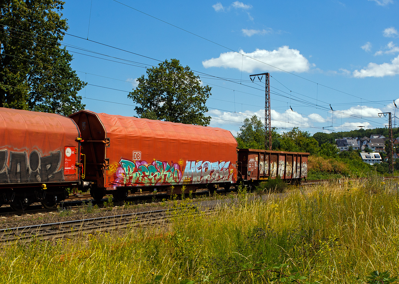 2-achsiger Flachwagen mit öffnungsfähigem Planendach und Stoßverzehreinrichtung zum Schutz vor Rangierstößen, 41 80 3384 088-5 D-DB, der Gattung Kijls 450, der DB Cargo AG (leider wie viele solcher Wagen sehr beschmiert), am 11 Juni 2024 im Zugverband bei einer Zugdurchfahrt durch Rudersdorf (Kreis Siegen) in Richtung Siegen bzw. Kreuztal.

Der Wagen wurde 2001 von ALSTOM LHB (vormals Linke-Hofmann-Busch GmbH in Salzgitter-Watenstedt gebaut.

Der Wagen lässt an sich einiges abprallen, er ist mit einer Stoßverzehreinrichtung zum Schutz vor Rangierstößen ausgestattet. So eignet sich dieser Wagen besonders zum Transport von stoßempfindlichen Gütern (z. B. Komponenten für die Automobilindustrie, Motoren, Getriebe, Maschinen, Trafos). Aufgrund des geschlossenen und verriegelten Planendachs gewährt er auch Schutz für nässeempfindliche Güter. Zusätzliche Zug-Spannsysteme gewährleisten eine schnellere Ladesicherung. Bei einer Ladelänge von über 14 Meter bietet der Wagen einen Laderaum von 109 m³.

Der Wagen besitzt einen unter dem Wagenkasten durchlaufenden, hydraulischen Stoßbalken, der die im Wagen befindlichen Güter weitgehend vor Rangierstößen schützt. Dadurch wird die auf die Ladung wirkende rechnerische Beschleunigung bei Auflaufgeschwindigkeiten bis 9 km/h auf 1 g (9,81 m/s²) begrenzt.

Die Stirnwände bestehen aus zwei schrägen Stirnwandsäulen, zwei Querträgern und einem Rahmen, der gleichzeitig das Dichtsystem aufnimmt. Die Dicke der Beblechung beträgt 2 mm. An den Stirnwänden sind die robusten 4-Punkt-Zentralverriegelungen angeordnet, mit der das Planendach zuverlässig gesichert werden kann. Die Betätigungseinrichtungen sind so angeordnet, dass das Ent- und Verriegeln des Planendaches sowohl vom Erdboden als auch von einer Rampe aus möglich ist. Die insgesamt 4 Verriegelungshaken (je Längseite) einschließlich der beiden Betätigungshebel sind über drehbar gelagerte Wellen untereinander verbunden. Dadurch ist ein Betätigen der Zentralverriegelung von jeder Wagenseite aus möglich.

Das Planendach besteht aus 2 End- und 10 Mittelspriegeln mit einer PVC-Beschichteten Gewebeplane. Die Spriegel ruhen auf Laufwagen, die wiederum selbst auf an den Langträgern angeordneten Fahrschienen stehen. Unter die Fahrschienen greifende Rollen an den Laufwagen wirken als Sicherungen und verhindern so ein Abheben der Hauben bei Auflaufstößen oder Windbelastung.

Das Planendach lässt sich mit geringem Kraftaufwand jeweils zu einem Wagenende hin verfahren und so weit zusammenschieben, dass ca. 3/4 der Ladelänge zur uneingeschränkten Beladung zur Verfügung stehen.

TECHNISCHE DATEN des Wagens:
Gattung: Gattung Kijls 450 (Gattungskennzahl 3384)
Erstes Baujahr: 2001
Spurweite: 1.435 mm (Normalspur)
Achsanzahl: 2
Länge über Puffer: 16.500 mm
Achsabstand: 10.000 mm
Ladelänge: 14.150 mm
Ladebreite: 2.850 mm
Ladefläche: 40,3 m²
Laderaum: 109 m³
Fußbodenhöhe über SOK: 1.2430 mm
Höchstgeschwindigkeit: 100 km/h (beladen) / 120 km/h (leer)
Eigengewicht: 17.450 kg
max. Zuladung: 27,5 t (ab Streckenklasse D) / DB Netz CM 24,5 t
Bauart der Bremse: KE-GP-A
Handbremse: nein
Intern. Verwendungsfähigkeit: nein
