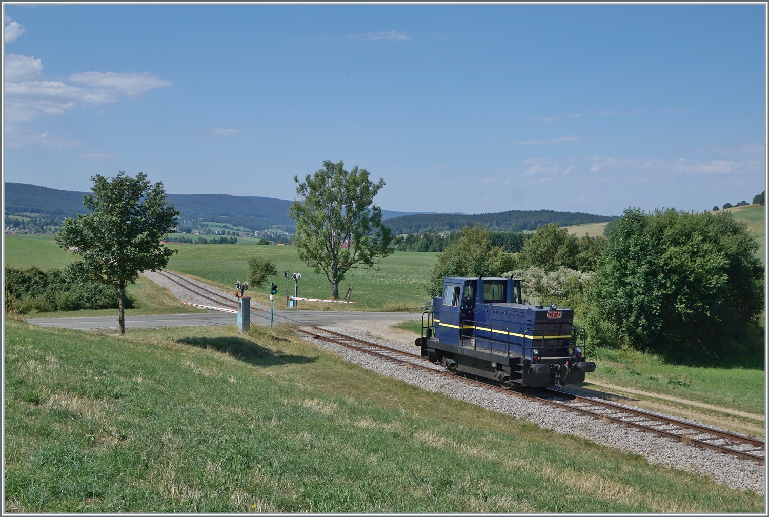 30 ANS CONI'FER /30 Jahre Coni'Fer - Nachdem der Coni'Fer locotracteur Tm 2/2 (ex TSOL Tm 2/2 238 291-9) die Coni'Fer  Orient Express  in Fontaine Ronde rangiert hat, wird die Lok wohl für das Manöver in Les Hôpitaux Neufs gebraucht, jedenfalls ist sie bei Le Touillon auf dem Weg dorthin. Das Bild zeigt auch einen Blick auf den Bahnübergang mit der Strasse D 45 und den entsprechenden Signalen und Ampeln für Strasse und Schiene.

15. Juli 2023