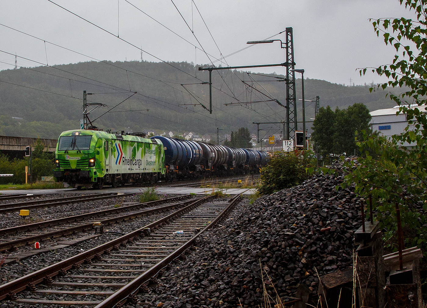 Bei Regen „Unterwegs mit Ökostrom“, die SIEMENS Smartron 192 056- 3 (91 80 6192 031-3 D-RHC), bzw. Lok 3001 der RheinCargo GmbH & Co. KG fährt man 03.08.2023 mit einem sehr langen Kesselwagenzug durch Niederschelden in Richtung Köln. Die Ladung der Kesselwagen war laut Gefahrgutkennzeichnung (30/1202) Dieselkraftstoff beziehungsweise leichtes Heizöl.

Die Smartron wurde 2020 von Siemens Mobilitiy in München-Allach unter der Fabriknummer 22889 gebaut. 
