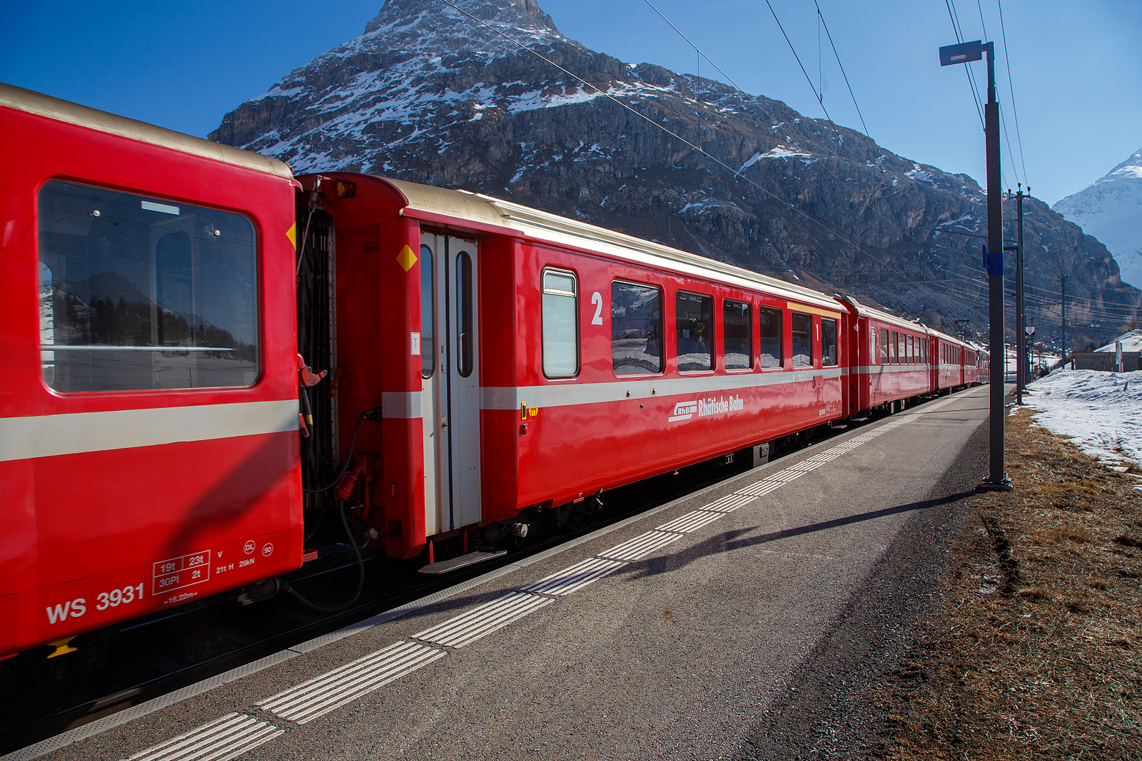 Berninabahn Personenwagen RhB AB 1545 (Baujahr 1968) ein verkrzter 1./2.Klasse Einheitswagen I (EW I) mit Aluminiumwagenkasten am 22.03.2023 in der Station Bernina Diavolezza (2.082 m . M.) im Zugverbund.

Mit mehr als 100 Fahrzeugen bilden die als Einheitswagen I bezeichneten Personenwagen bis heute die grte Serie im Rollmaterialbestand der RhB. Das Fahrzeugkonzept wurde Anfang der sechziger Jahre in enger Zusammenarbeit zwischen Industrie und RhB entwickelt. Als Neuheit galten damals die Einstiegsbereiche mit WC und Stauraum fr sperriges Gepck an den Wagenbergngen. Folglich weicht das Konzept deutlich von den Mitteleinstiegswagen aus den vierziger Jahren ab.

Die ersten von FFA und SIG gebauten Einheitswagen I wurden Ende 1963 in Betrieb genommen. In einem Zeitraum von etwa zehn Jahren wuchs der Bestand an EW I kontinuierlich. Neben den 18,42 m langen Wagen, die hauptschlich auf dem Stammnetz eingesetzt werden, kamen auch Sonderbauformen mit Aluminiumwagenkasten hinzu. Zu diesen zhlen beispielsweise diese auf 14,91 m verkrzten Fahrzeuge fr den Einsatz auf der Berninabahn. Um auch die dort engen 50 m Radien befahren zu knnen, wurden die Wagen AB 1541-1546 bzw. B 2307-2314 sowie B 2451-2460 deutlich lngenverkrzt ausgefhrt. Die Fahrzeuge werden heute noch in vielen Regionalzgen auf der Berninalinie eingesetzt, sie laufen aber auch auf dem Stammnetz und haben zudem eine Zulassung fr die benachbarten MGB (ex FO/BVZ). 

TECHNISCHE DATEN:
Baujahr und Hersteller: 1968 / Flug- und Fahrzeugwerke Altenrhein AG (FFA)
Spurweite: 1.000 mm
Anzahl der Achsen: 4
Lnge ber Puffer: 14.910 mm
Drehgestellart: SWP 68
Sitzpltze: 12 (1.Klasse) / 30 (2.Klasse)
Eigengewicht: 14,0 t
Max. Gesamtgewicht: 17 t
zulssige Geschwindigkeit: 90 km/h
Lauffhig: StN (Stammnetz) / BB (Berniabahn) / MGB (Matterhorn Gotthard Bahn)
