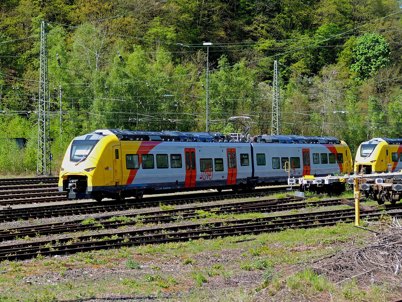 Das ist der neue Klimaschutz am Westerwald....
Zwei der drei neuen zweiteiligen Hybridtriebzüge (E/Akku) der BR 563 vom Typ SIEMENS Mireo Plus B der HLB (Hessische Landesbahn GmbH) sind am 30 April 2025 in Betzdorf/Sieg abgestellt. Links der 563 801/563 901 (94 80 0563 801-0 D-HEB / 94 80 0563 901-8 D-HEB) und rechts daneben der 563 803/563 903 (94 80 0563 803-6 D-HEB / 94 80 0563 903-4 D-HEB)

Die beiden zweiteiligen SIEMENS Mireo Plus B wurden 2024 von SIEMENS in Krefeld gebaut. 

Auszug aus der Pressemitteilung der HLB:
Alternative Antriebe im Norden von Rheinland-Pfalz: Durchbruch beim Pilotprojekt mit Batteriezügen im Westerwald / Zuschlag an Siemens Mobility für Mireo Plus B Fahrzeuge

Als Aufgabenträger für den Nahverkehr auf der Schiene im Norden von Rheinland-Pfalz setzt sich der SPNV-Nord gemeinsam mit seinen Projektpartnern von Bund, Land und Eisenbahnverkehrsunternehmen (EVU) für den Einsatz von alternativen Antrieben als Abkehr vom Dieselbetrieb ein.

Dabei konnte bereits im letzten Jahr für die Beschaffung der Fahrzeuge eine Unterstützung aus dem Förderprogramm des Bundesministeriums für Digitales und Verkehr (BMDV) für alternative Antriebe gewonnen werden.

Als Besonderheit sollen im SPNV-Nord erstmalig die beiden Antriebstechnologien für die Dekarbonisierung des Schienenverkehrs, Wasserstoff und Batterieelektrik, nebeneinander im mehrjährigen Fahrgastbetrieb zum Einsatz kommen mit einer vollständigen Rückfallebene mit Dieselfahrzeugen.

Das betrifft auch den Pilotbetrieb mit drei batterie-elektrischen Fahrzeugen im Westerwald, der zum Fahrplanwechsel im Dezember 2025 geplant ist. Dieser sieht einen Fahrzeugeinsatz auf der RB 90 Limburg – Au – Siegen (Oberwesterwaldbahn und Siegstrecke) und auf der RB 29 Limburg – Siershahn (Unterwesterwaldbahn) durch die Hessische Landesbahn (HLB) vor. Bei diesem Pilotprojekt wurde jüngst ein wichtiger Durchbruch erzielt:

Als Ergebnis der von der HLB dafür durchgeführten Fahrzeugausschreibung hat Siemens Mobility jetzt den Zuschlag für drei zweiteilige Mireo Plus B Batteriezüge erhalten. Das Fahrzeug mit seiner hohen Antriebsleistung ist für den anspruchsvollen Einsatz im Westerwald bestens geeignet. Der geplante Einsatz der drei Batteriezüge auf den Linien RB 90 und RB 29 umfasst eine Jahresfahrleistung von fast 400.000 Zug-km und ersetzt drei Dieselfahrzeuge. Da die HLB emissionsfreien Bahnstrom bezieht, werden jährlich fast 1.150 Tonnen CO2 eingespart. Der Betrieb der Batteriefahrzeuge erfordert keine neue Infrastruktur, denn die Wendezeiten in Limburg von über 20 Minuten auf der RB 29 werden für die Aufladung der Fahrzeuge ausreichend sein. Bei den auf der RB 90 verkehrenden Batteriefahrzeugen erfolgt dies im elektrifizierten Abschnitt zwischen Au und Siegen. Die Oberwesterwaldbahn (Limburg – Au) ist mit der Länge von rund 75 km und der zu überwindende Höhe von ca. 350 m derzeit in Deutschland die anspruchsvollste Strecke für den vorgesehenen Einsatz von Batteriezügen.

Die Ausschreibung der Batteriefahrzeuge war so ausgestaltet, dass die Hersteller die Möglichkeit hatten, die Fahrzeuge in laufende Bestellungen zu integrieren, so dass eine schnelle Lieferzeit in Aussicht gestellt wurde.

Siemens Mobility baut für den Einsatz im Westerwald drei zweiteilige Mireo Plus B Batteriezüge, die durch jeweils drei Türen pro Seite einen schnellen Ein- und Ausstieg ermöglichen. Die Züge verfügen für den Betrieb unter Oberleitung und zum Aufladen der Batterien über einen Stromabnehmer und verkehren auf den nicht-elektrifizierten Strecken im Batteriebetrieb. Die geräumigen Fahrzeuge bieten den Fahrgästen 126 Sitzplätze und 156 Stehplätze und sind mit einer speziellen Einstiegshilfe ausgestattet, die mobilitätseingeschränkten Menschen das Bahnfahren erleichtert.

Die neuen Batteriezüge werden auf der Oberwesterwaldbahn Limburg – Altenkirchen - Au - Siegen, und auf der Unterwesterwaldbahn zwischen Limburg – Montabaur – Siershahn unterwegs sein. Die Strecke der OWB beträgt ca. 115 km, davon sind ca. 75 km ohne Fahrdraht. Es ist vorgesehen die Züge in Limburg und auf dem Teilabschnitt Au – Siegen nachzuladen. Auf der UWB beträgt die nicht elektrifizierte Strecke ca. 35 km. Damit ist ein Zugbetrieb hin und zurück ohne Nachladen möglich. Insgesamt werden die Züge über 50 Bahnhöfe anfahren.

TECHNISCHE DATEN:
Spurweite: 1.435 mm
Achsfolge: Bo’-2’-Bo’
Fahrzeuglänge über Kupplung: 46.560 mm
Drehzapfenanstand: 2 x 17.930 mm
Anzahl der Türen je Seite: 3
Installierte Leistung: 1.700 kW
Leistungsübertragung: elektrisch
Motoren: 2 Drehstrom-Asynchronmotoren
Höchstgeschwindigkeit: 140 km/h 
Kupplung: Mittelpufferkupplung Schaku Typ 10
kleinster befahrbarer Gleisbogen: R 150 m (Normal) / R 100 m (Werkstatt)

Ein kleiner Nachteil gegenüber den LINT-Dieseltriebzügen ist mir aufgefallen, die Gesamt-Fensterfläche ist geringer. Ich bin aber sehr gespannt auf den Betriebseinsatz und wie es läuft.
