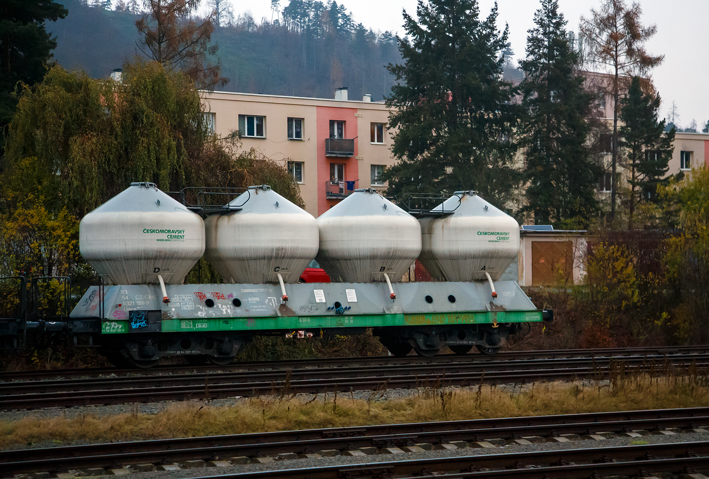 Der 4-achsiger Drehgestell-Silo-/Zementwagen 83 54 9321 181-9 CZ-CMC, der Gattung Uacs 451.1,der tschechischen Českomoravský cement, a.s., gehört zur HeidelbergCement Group, abgestellt am 24.11.2022 bei Karlštejn (deutsch Karlstein, zum Bezirk Beroun). Aufnahme aus dem Zug heraus. Die vier Behälter haben jeweils ein Ladevolumen von 13 m³ = 52 m³ Gesamtvolumen. Das max. Ladegewicht beträgt 47,6 t ab Streckenklasse B bei Lastgrenze S (100 km/h), in CZ auch 56,6 t ab Streckenklasse C bis 90 km/h möglich.

Die Bedeutung der Gattungs- und Kennbuchstaben (hier Uacs):
U - Sonderwagen 
a - mit vier Radsätzen
c - mit Entladung unter Druck
s - Höchstgeschwindigkeit 100 km/h (beladen)
