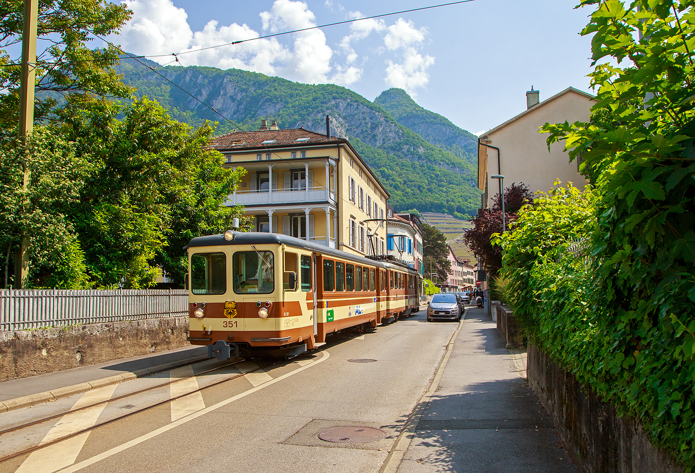 Der AL Regionalzug von Leysin nach Aigle fährt am 28. Mai 2023 (hier als Straßenbahn) durch Altstadt und erreicht bald den Bahnhof Aigle. Der Zug besteht aus dem führenden Steuerwagen AL Bt 351 „Aigle“  und dem Triebwagen AL BDeh 4/4 302 „Leysin“, beide sind noch im ursprünglichen Anstrich der AL (es sind auch die einzigen). 

In Aigle (Waadt) gibt es gleich drei Schmalspurbahnen, die seit 1999 in die Transports Publics du Chablais (TPC) fusioniert worden sind, so machten wir auf unserer Rückreise hier mal einen kurzen Zwischenhalt. Die Schmalspurbahnen sind die Aigle–Ollon–Monthey–Champéry-Bahn (AOMC), die Aigle–Sépey–Diablerets-Bahn (ASD), seit dem 22. Dezember 1913 und die Aigle–Leysin-Bahn (AL).

Die Chemin de fer Aigle–Leysin (AL), deutsch Aigle-Leysin-Bahn, war eine Eisenbahngesellschaft im Schweizer Kanton Waadt. Ihre von 1900 bis 1916 eröffnete 6,2 Kilometer lange Strecke führt von Aigle im Rhonetal hinauf nach Leysin-Grand Hôtel. Die gemischte Zahnradbahn in der Spurweite 1.000 mm (Meterspur) mit dem System Abt wird seit der Betriebsaufnahme elektrisch betrieben. Im Jahr 1999 fusionierte die AL zu den Transports Publics du Chablais (TPC).

Die Bahnstrecke Aigle–Leysin hat ihren Ausgangspunkt vor dem SBB-Bahnhof und führt als Straßenbahn auf der Rue de la Gare (Bahnhofstraße), der Avenue des Ormonts und über die Grande Eau zum Kopfbahnhof Aigle-Dépôt. Dort ändern die Züge die Fahrtrichtung, damit das Triebfahrzeug für die anschließende Bergfahrt am Ende des Zuges eingereiht ist. 

Im Keilbahnhof Aigle-Dépôt beginnt der 5,3 Kilometer lange und bis zu 230 Promille steile Zahnstangenabschnitt. Zunächst führt er durch die Rebberge und bietet den Fahrgästen einen Ausblick auf das Rhonetal. Bei der Haltestelle Pont-de-Drapel wechselt die Vegetation und das Trassee befindet sich nun im Wald. Der Zug erreicht eine Waldlichtung mit dem Bahnhof Rennaz (Leysin), wo er sich in der Regel mit dem Gegenzug kreuzt. Die Strecke führt weiter durch Wald und den 154 Meter langen Tunnel Rennaz. Ab rund 1.200 Meter über Meer fährt die Zahnradbahn durch Weiden und erreicht nach kurzer Zeit den Bahnhof Leysin-Village (Leysin-Dorf). Hier beginnt der Doppelspurabschnitt mit der 128 Meter langen Brücke Leysin nach Leysin-Feydey. Nach dem 287 Meter langen Kehrtunnel Leysin erreicht die Strecke, immer noch mit Zahnstange versehen, den Endpunkt Leysin-Grand Hôtel.


Die Triebwagen und Steuerwagen BDeh 4/4 301–302 und Bt 351–352 wurden 1966 von SIG/SAAS gebaut. 

TECHNISCHE DATEN:
Spurweite: 1.000 mm
Fahrleitungsspannung: 1.500 V =

Triebwagen: BDeh 4/4 301-302
Zahnstangensystem: Abt
Achsfolge: Bo'zz Bo'zz
Länge über Puffer: 16.100 mm
Drehzapfenanstand: 9.540 mm
Achsabstand im Drehgestell: 2.460 mm
Leistung: 596 kW (808 PS)
Treibraddurchmesser: 840 mm (neu)
Zahnrad-Teilkreisdurchmesser: 650
Höchstgeschwindigkeit: 40 km/h
Übersetzung: 1:12,2
Gewicht: 33.0 t
Sitzplätze: 48
Max. Ladegewicht: 1,5 t

Steuerwagen Bt 351–352
Anzahl der Achsen: 4
Gewicht: 11.0 t
Sitzplätze: 48
