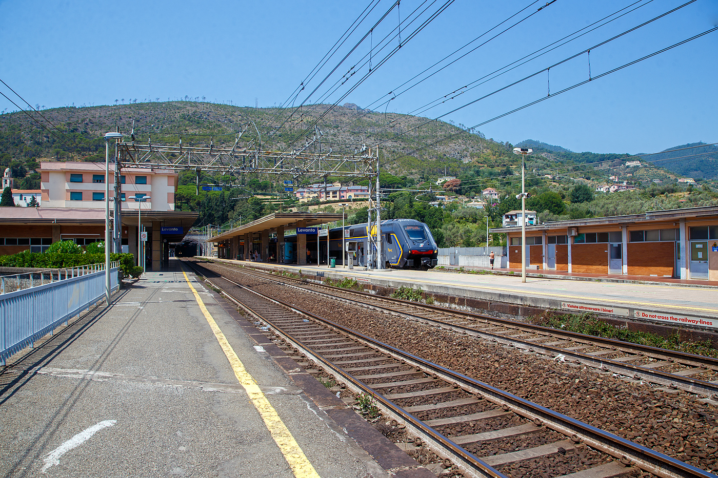 Der Bahnhof Levanto an der Italienischen Riviera (nördlich der Cinque Terre) am 22.07.2022. Der Bahnhof liegt an der Bahnstrecke Pisa–Genua (RFI Strecke-Nr. 77 / KBS 31 La Spezia–Genua),

Rechts steht der Trenitalia “Rock” ETR 521-021, ein fünfteiliger Elektrotriebzug vom Typ Hitachi Caravaggio, als Cinque Terre Express (Regionale 22923) Levanto, via Monterosso, Vernazza, Corniglia, Manarola und Riomaggiore nach La Spezia bereit. Während durch den Tunnel gerade zwei gekuppelte Trenitalia „pop“ (ETR 104) aus Richtung Sestri Levante kommen.